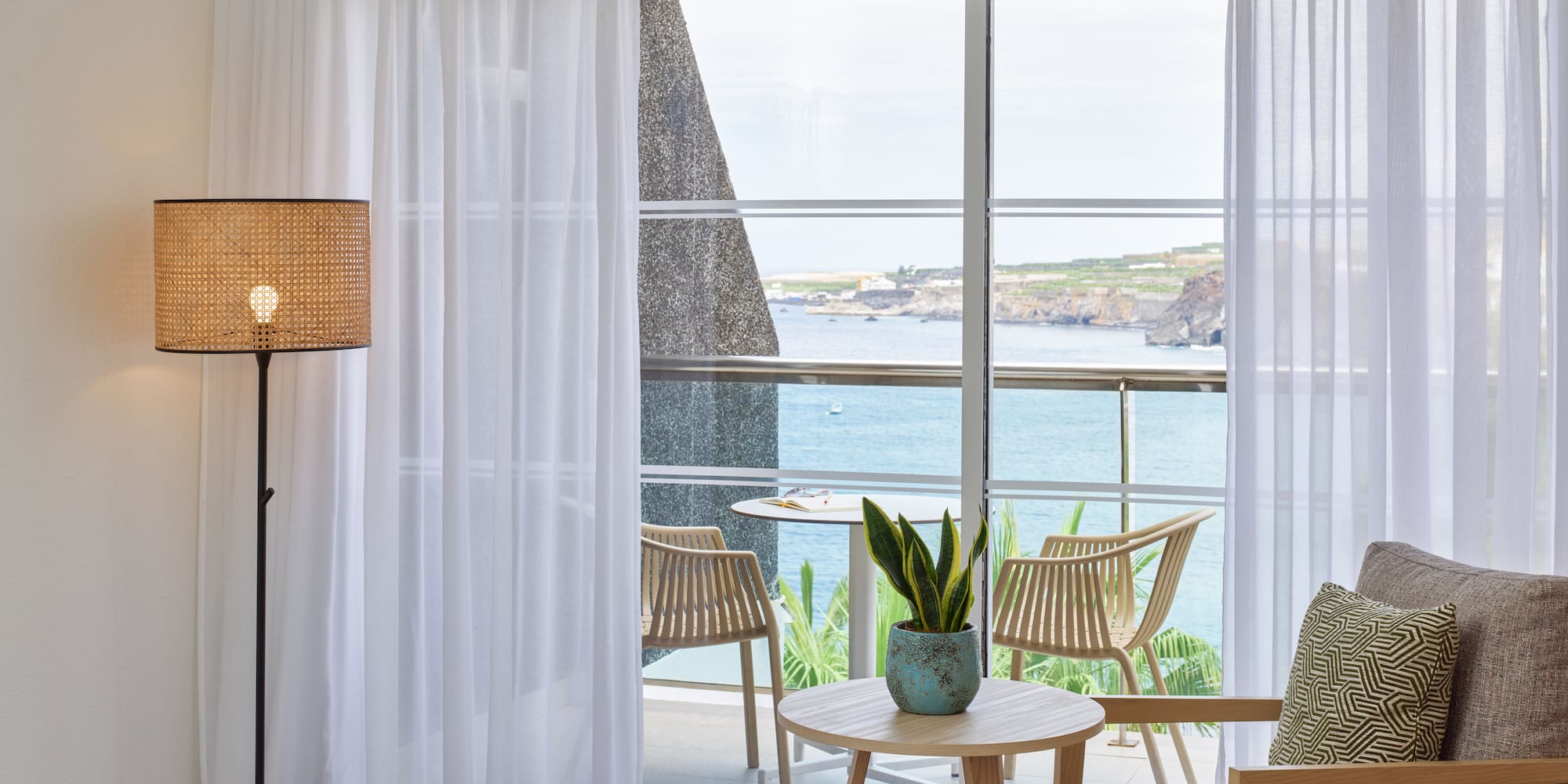 a room with a bed and chairs and a table with a view of the ocean
