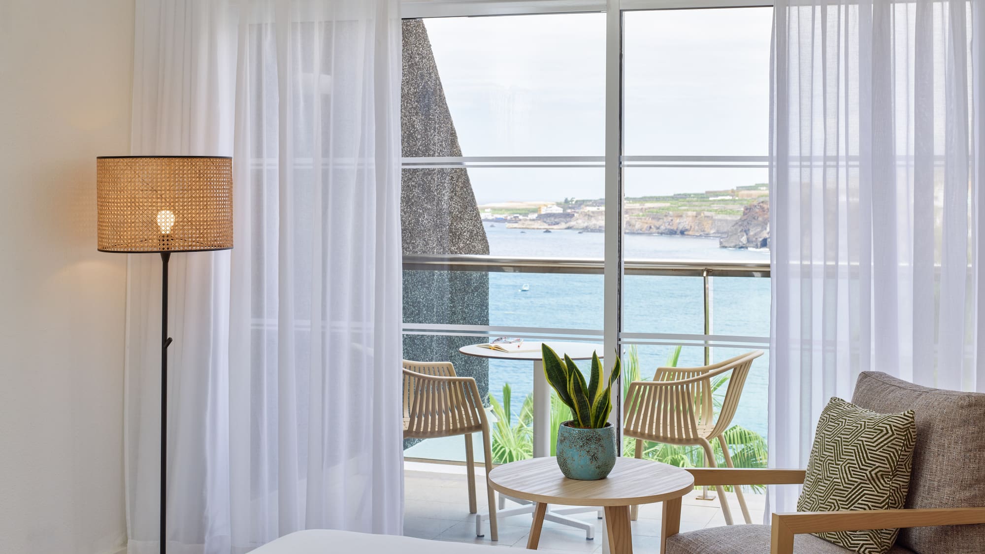 a room with a bed and chairs and a table with a view of the ocean