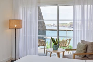 a room with a bed and chairs and a table with a view of the ocean