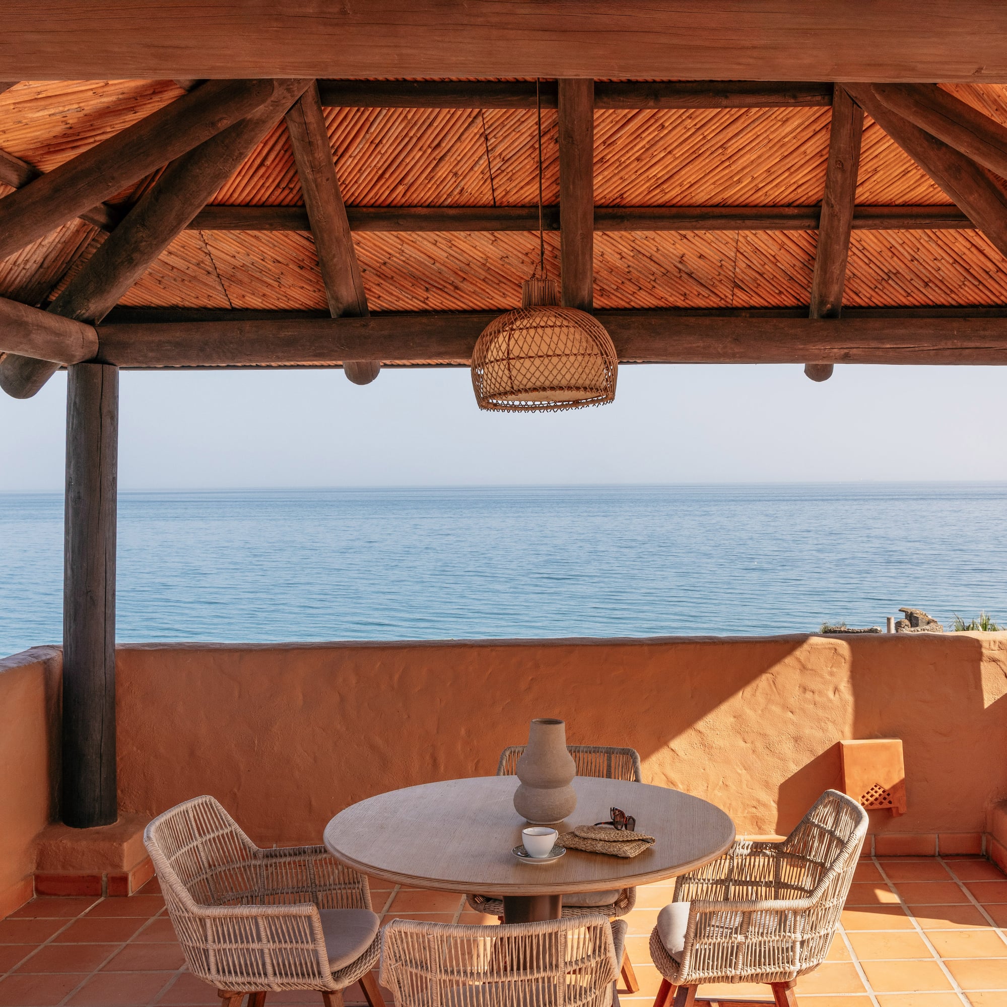 Ocean view resort terrace with wooden pergola and outdoor dining set.