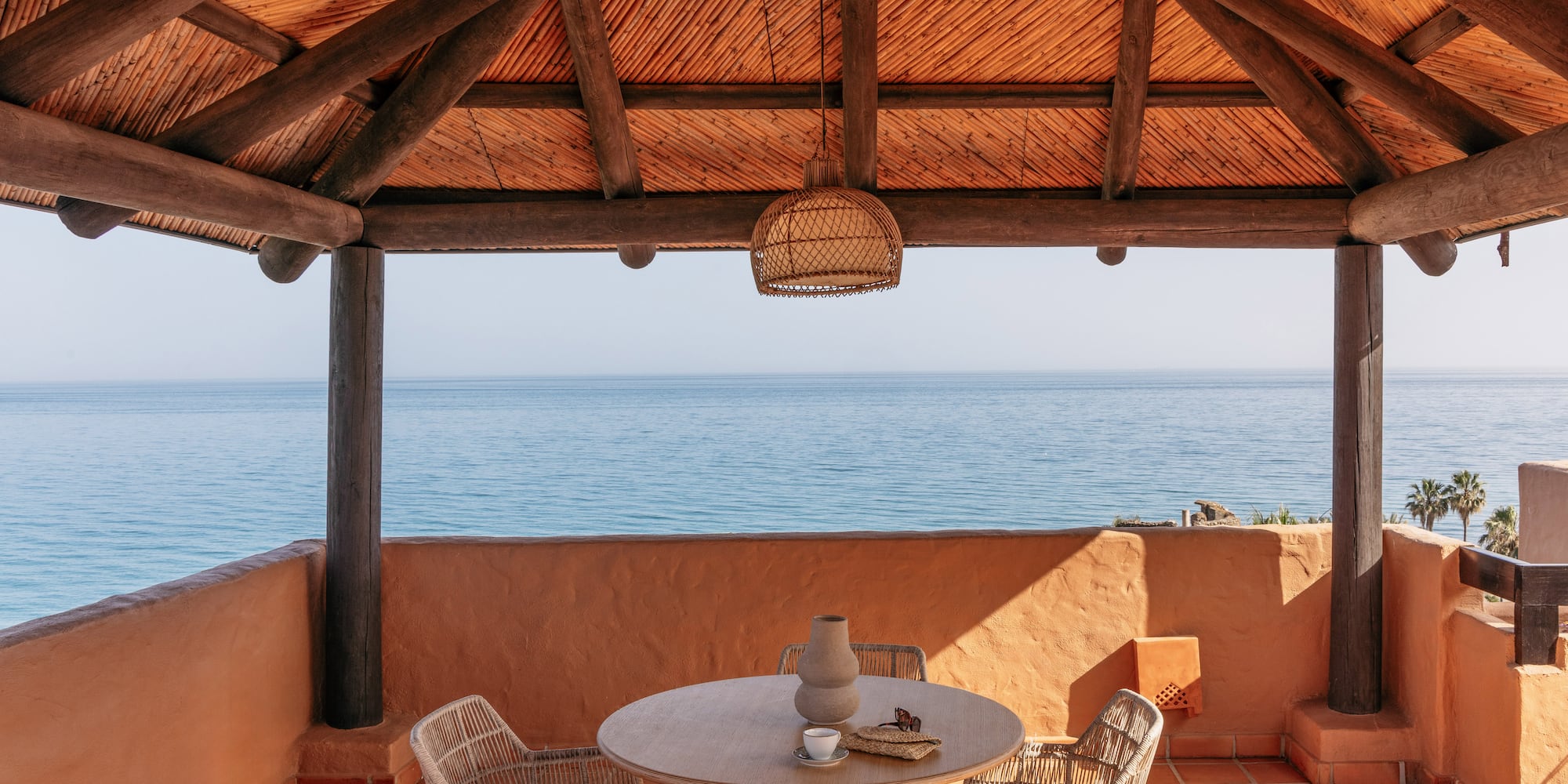 Ocean view resort terrace with wooden pergola and outdoor dining set.