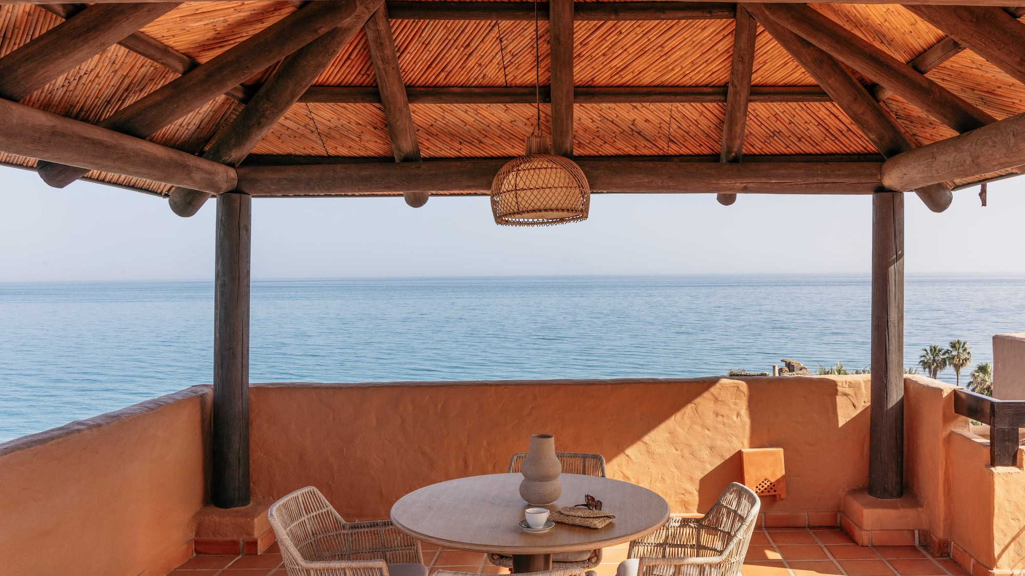 Ocean view resort terrace with wooden pergola and outdoor dining set.
