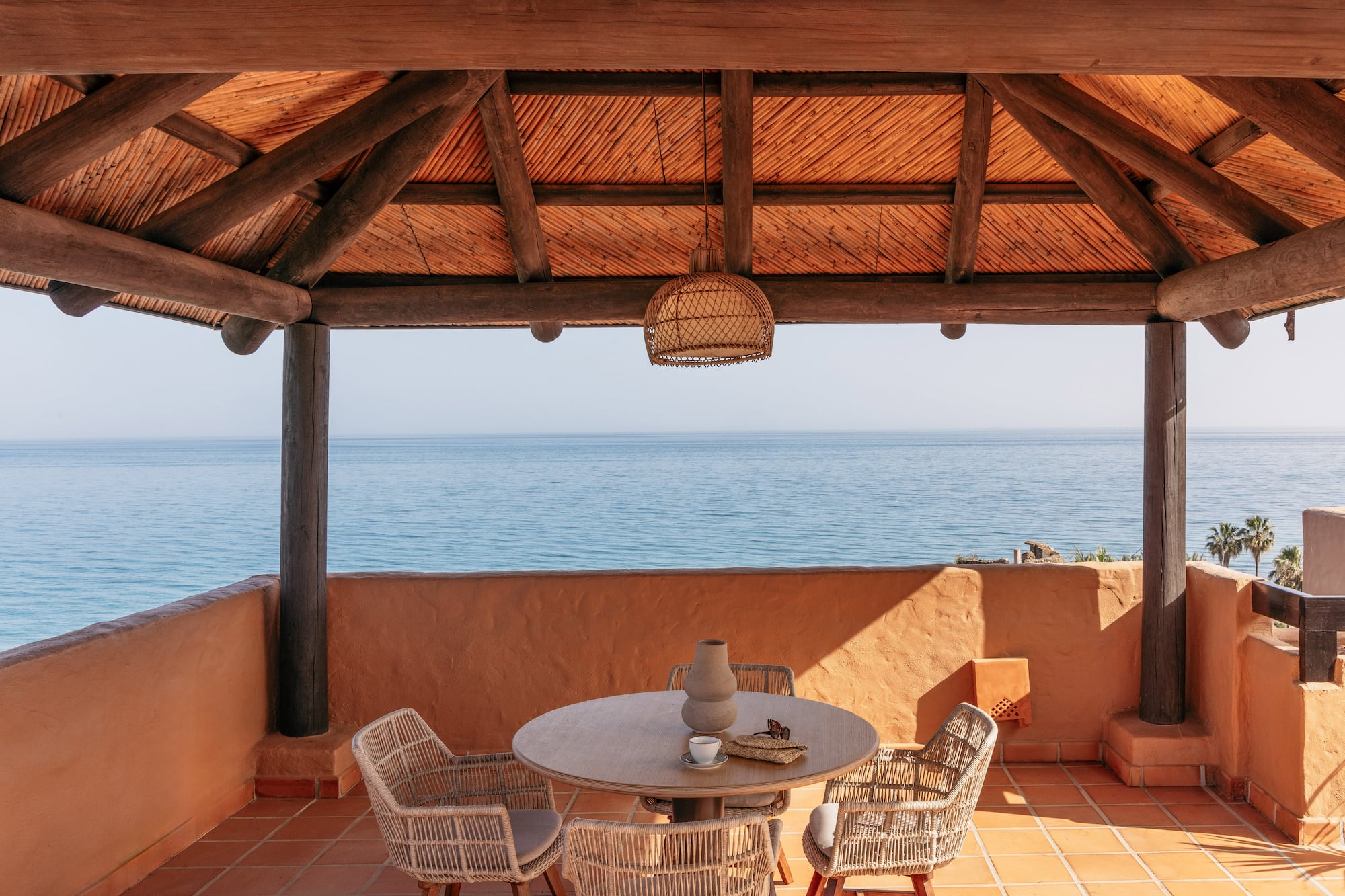 Ocean view resort terrace with wooden pergola and outdoor dining set.