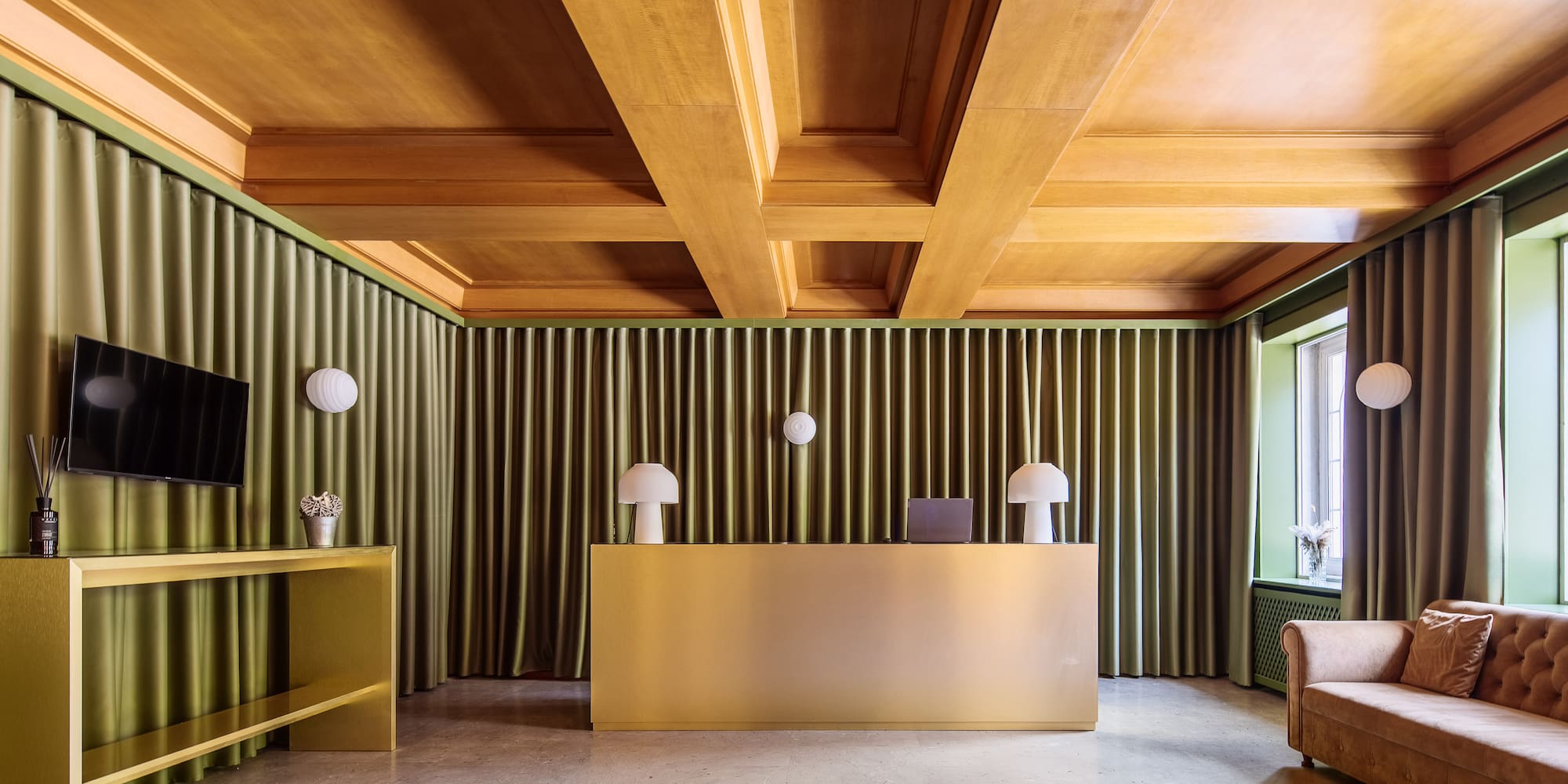 Elegant hotel lobby with golden reception desk, green curtains, wooden ceiling.