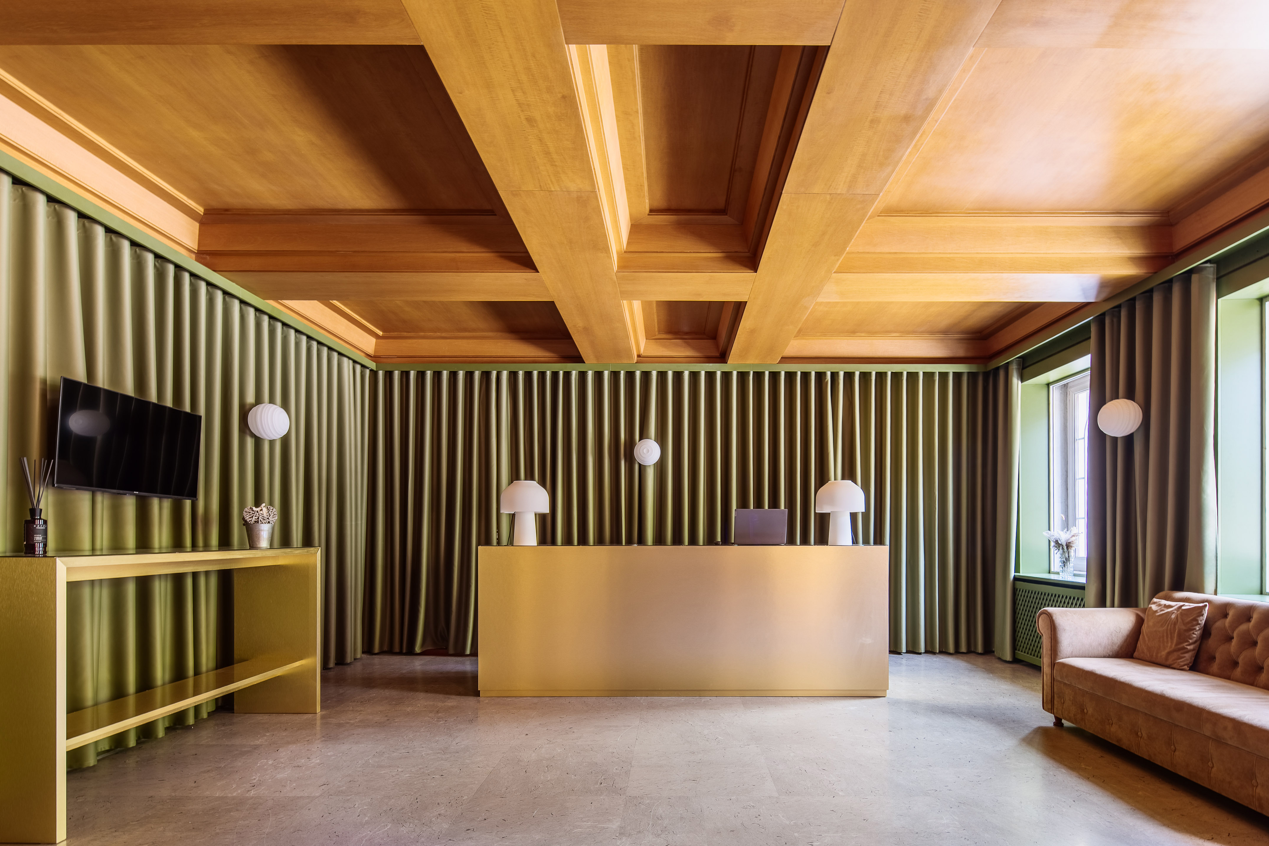 Elegant hotel lobby with golden reception desk, green curtains, wooden ceiling.
