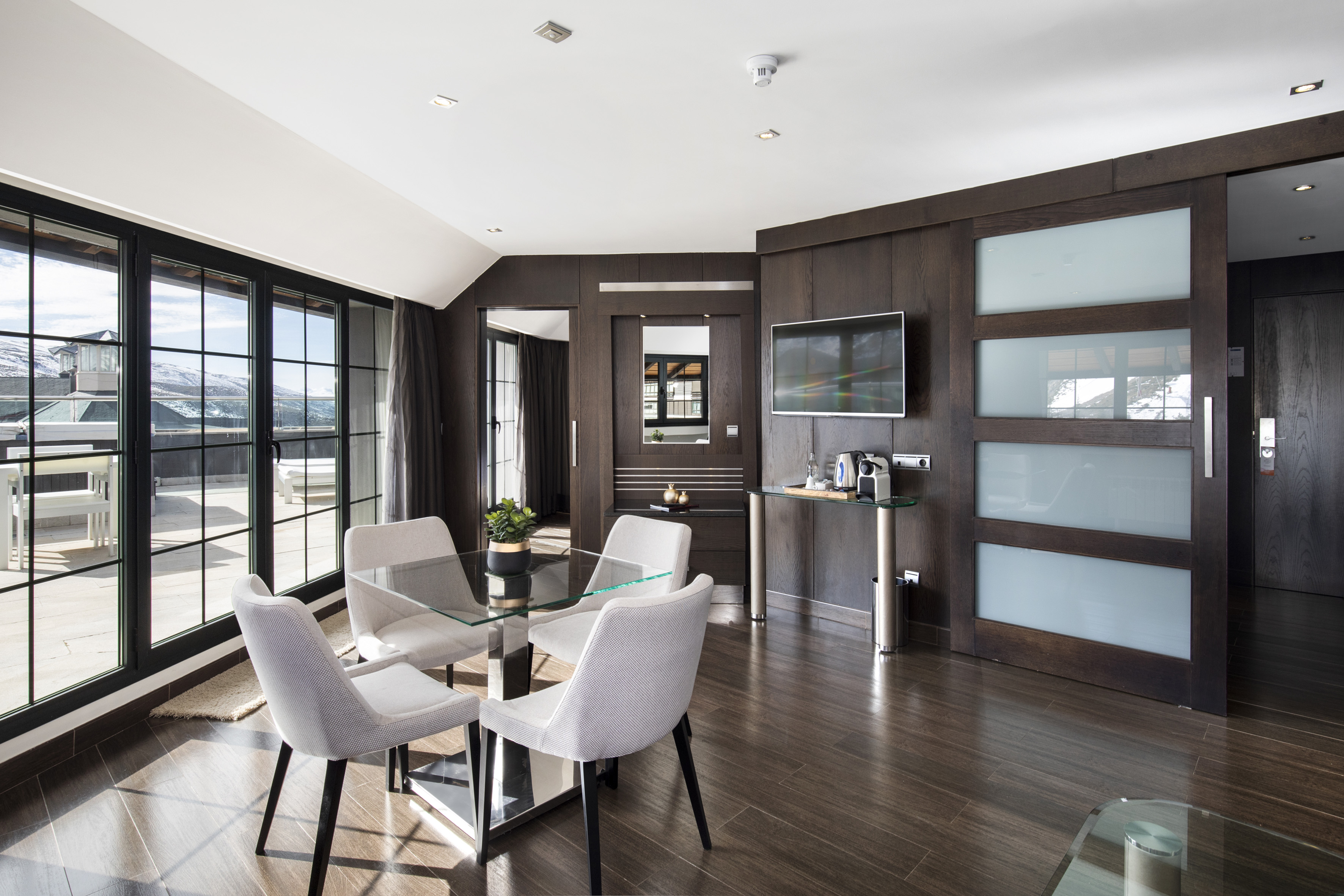 Modern luxury suite with dining table, large windows overlooking snowy mountains.
