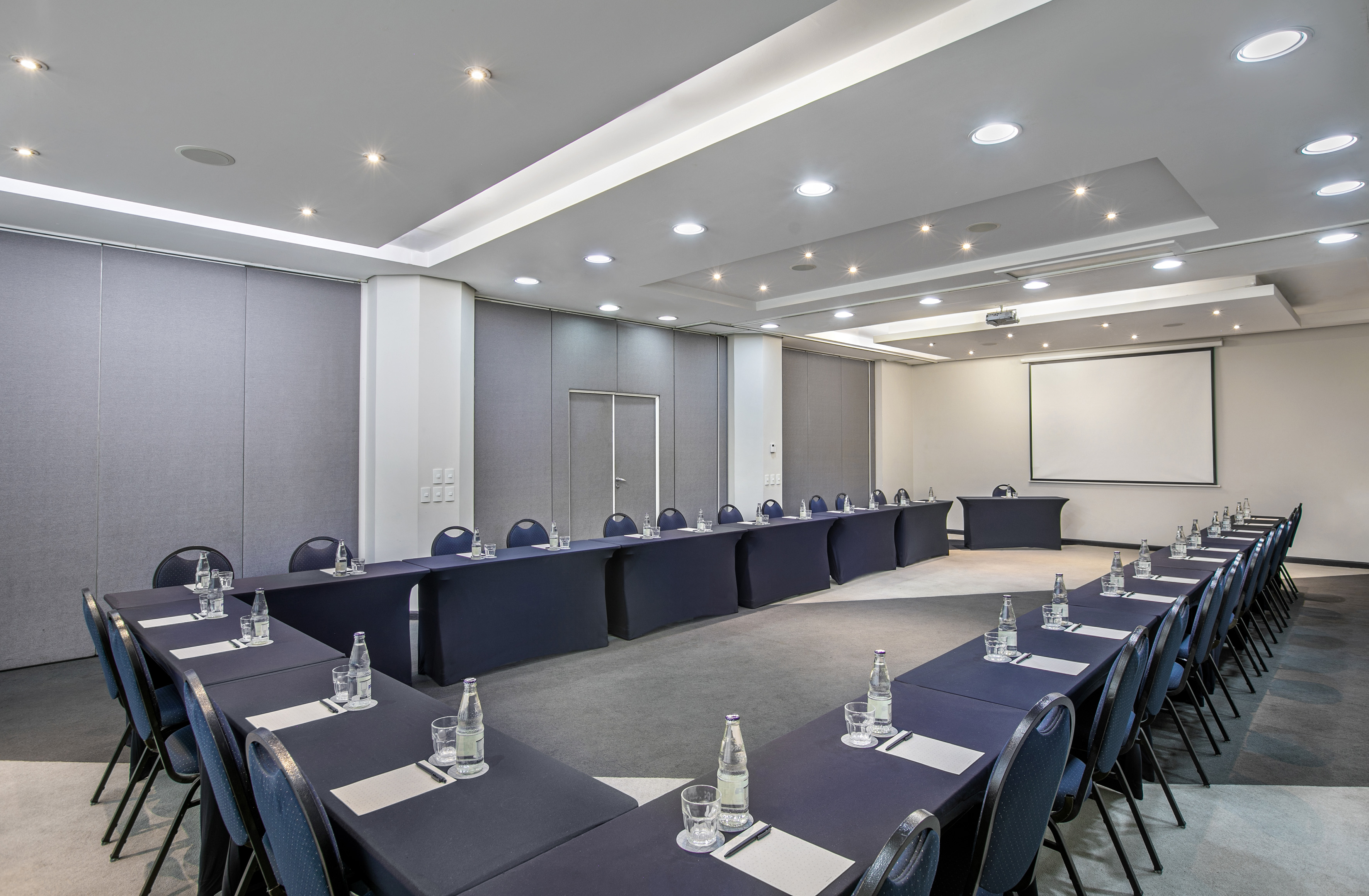 Modern conference room with U-shaped table setup and projector screen.