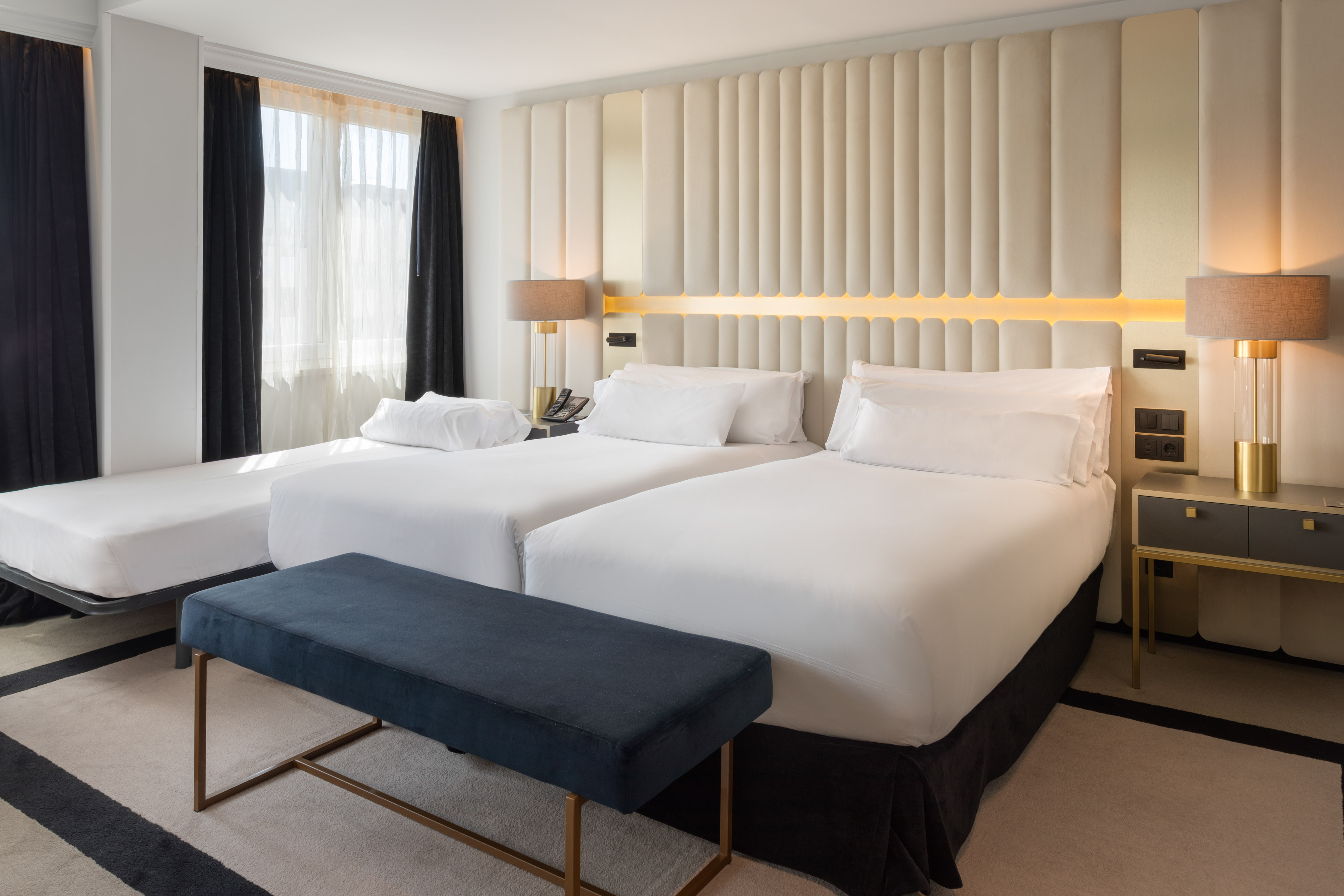 Modern hotel twin room with extra bed and elegant padded headboard.