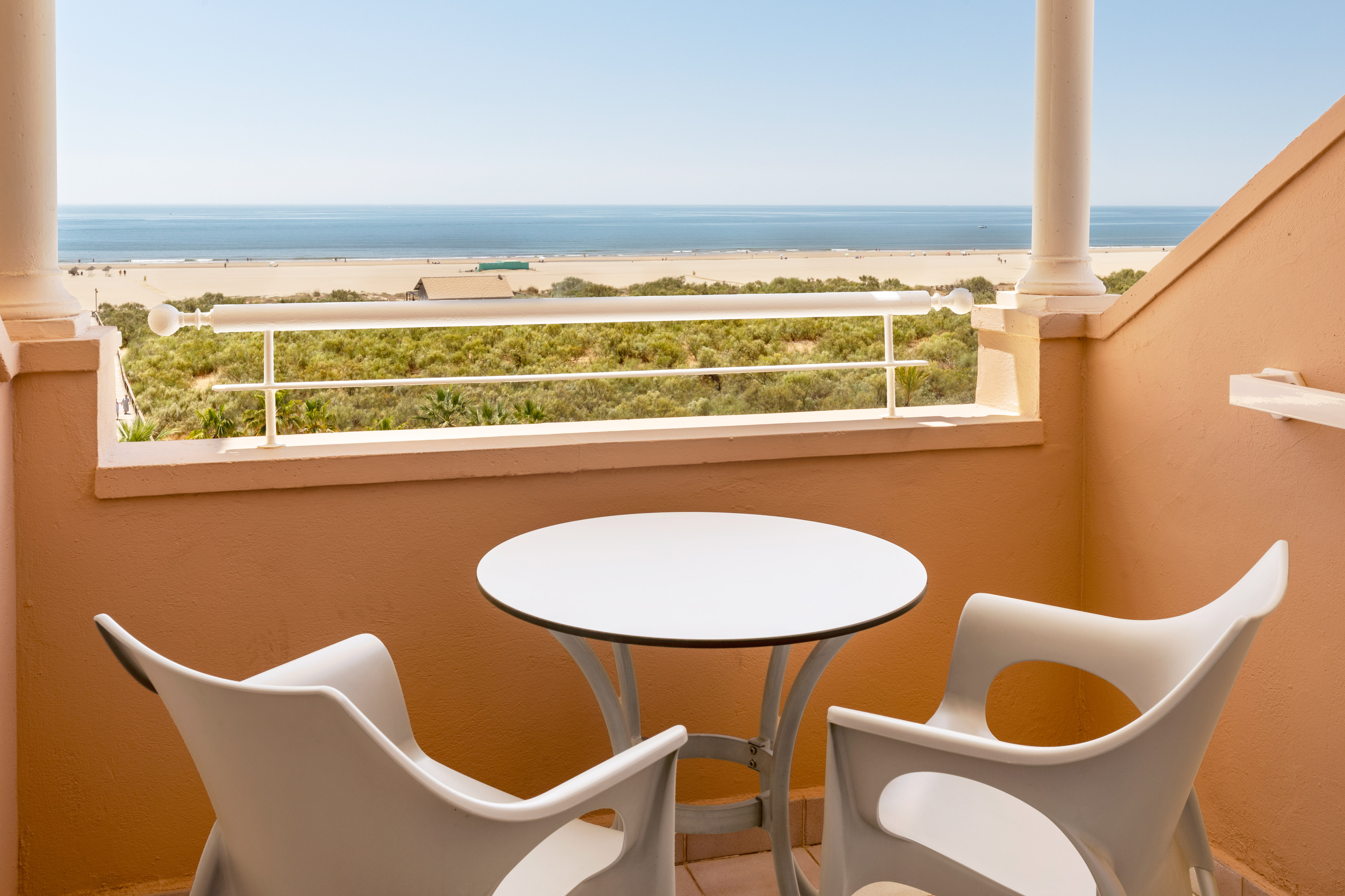 Balcony with white table, chairs, overlooking sandy beach and ocean.
