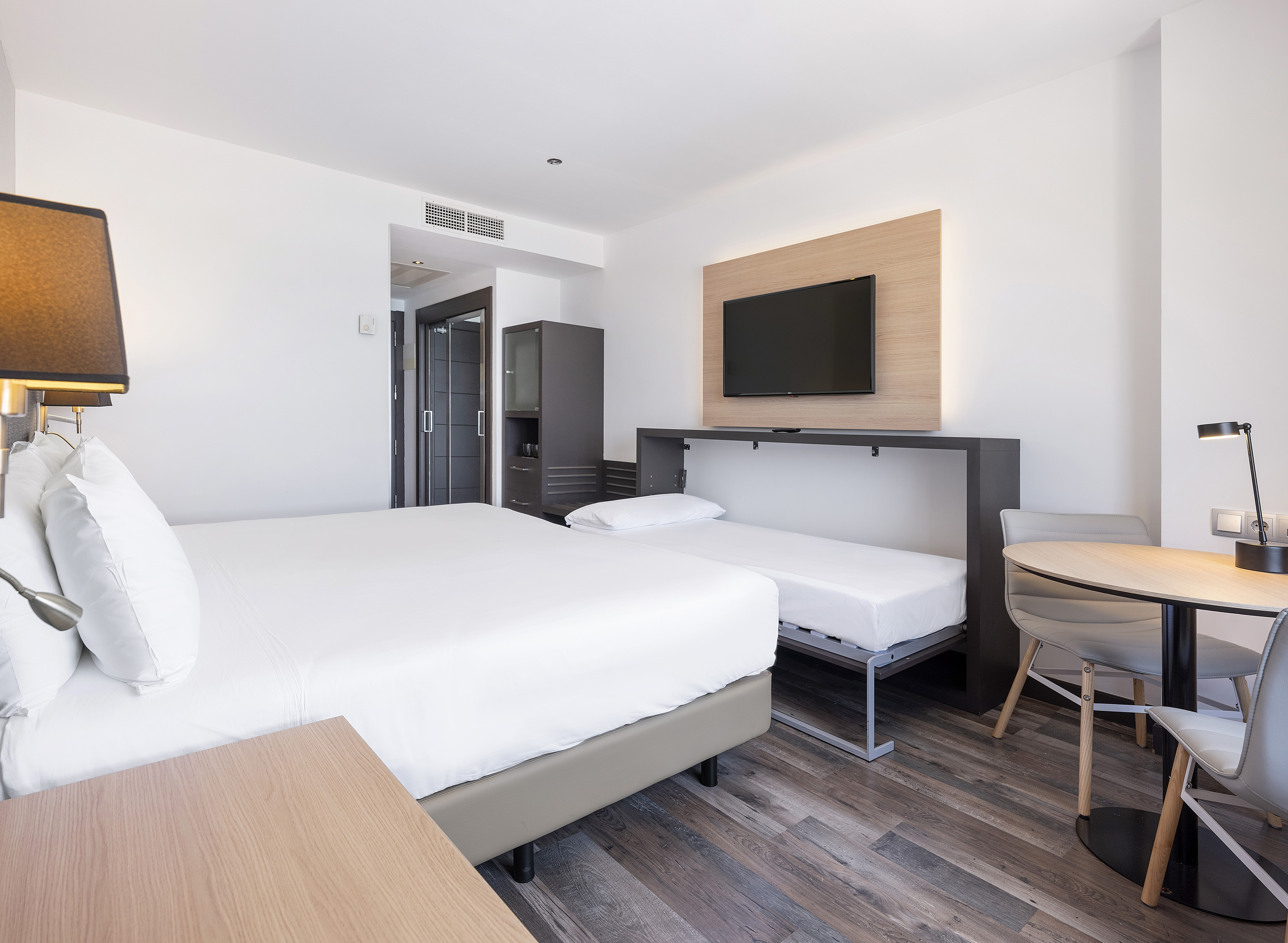 Modern hotel room with double bed, pull-out bed, TV, and dining table.