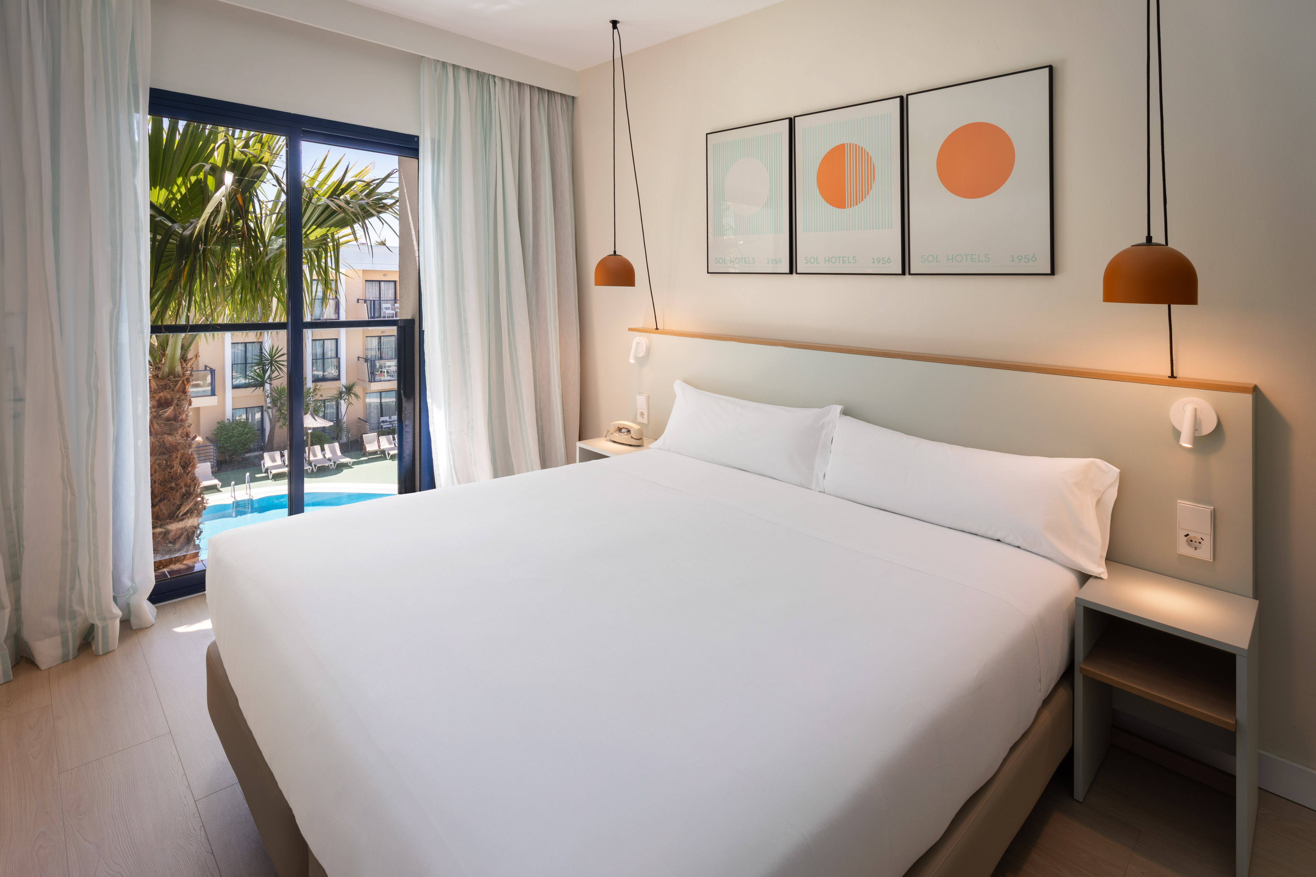 Modern hotel room with king bed, pool view, palm trees, and contemporary decor.