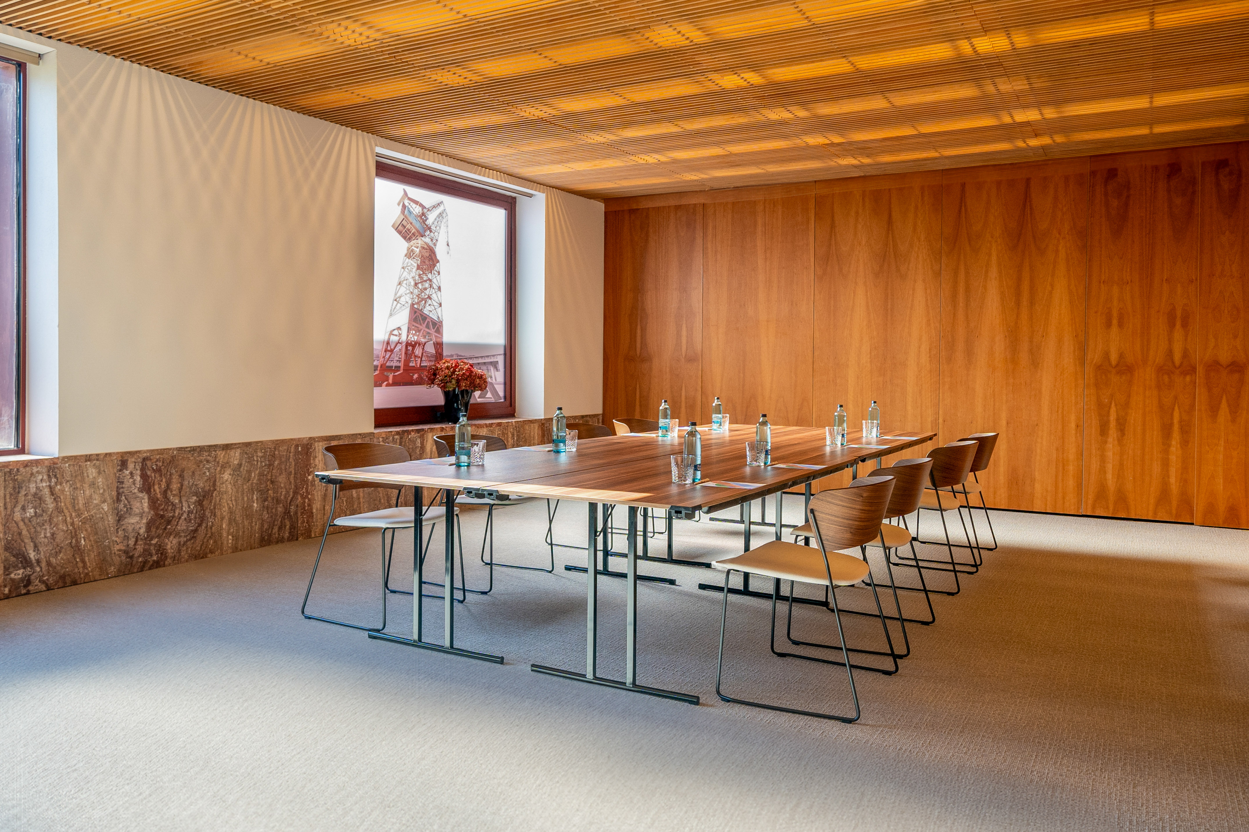 Modern conference room with wooden table, chairs, wood walls, and slatted ceiling.