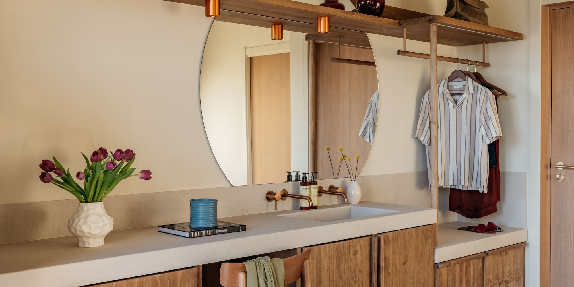 Modern bathroom vanity, round mirror, copper fixtures, and built-in storage.