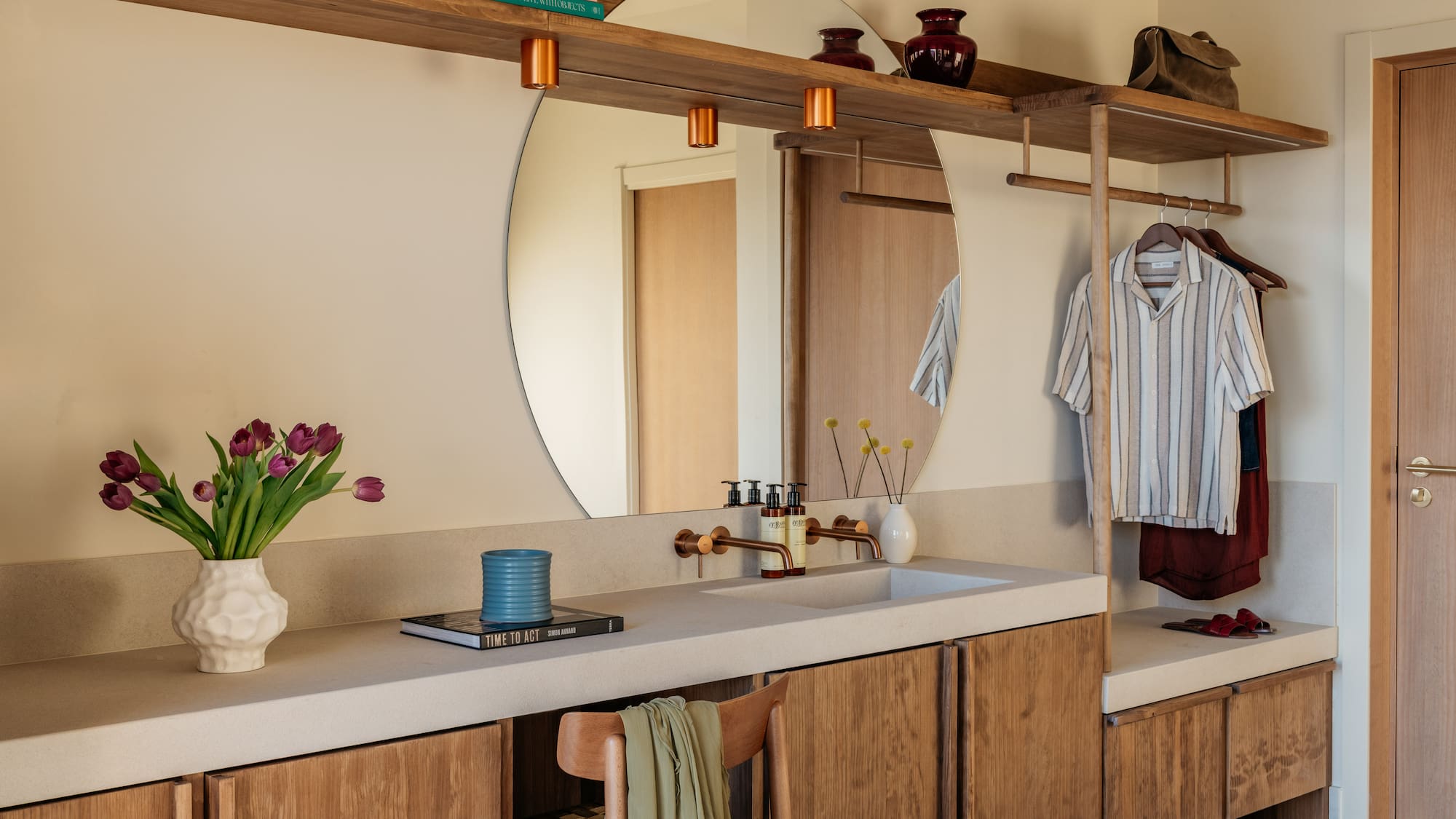 Modern bathroom vanity, round mirror, copper fixtures, and built-in storage.
