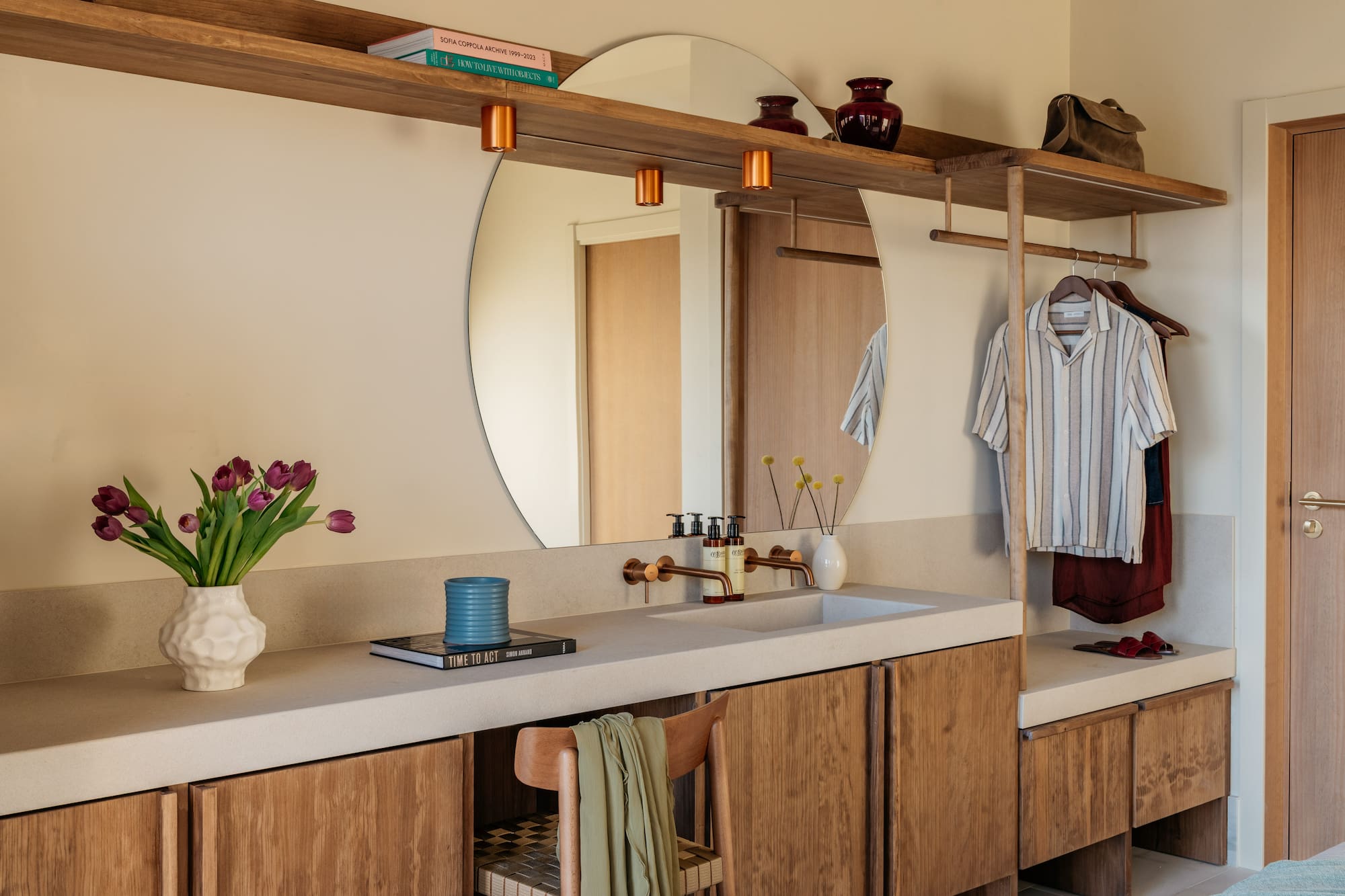 Modern bathroom vanity, round mirror, copper fixtures, and built-in storage.