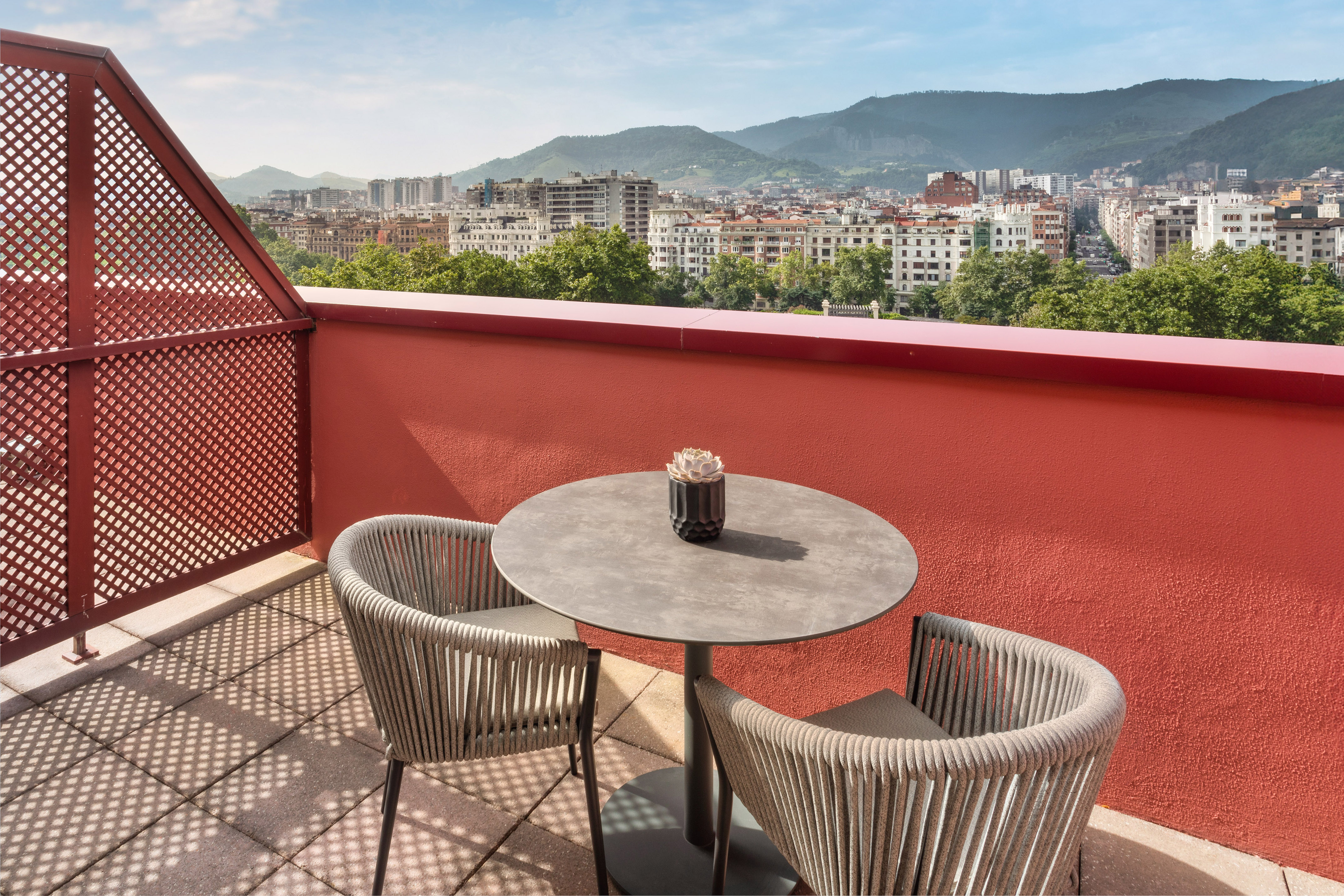 Hotel balcony with table, chairs, city skyline, and mountain views.
