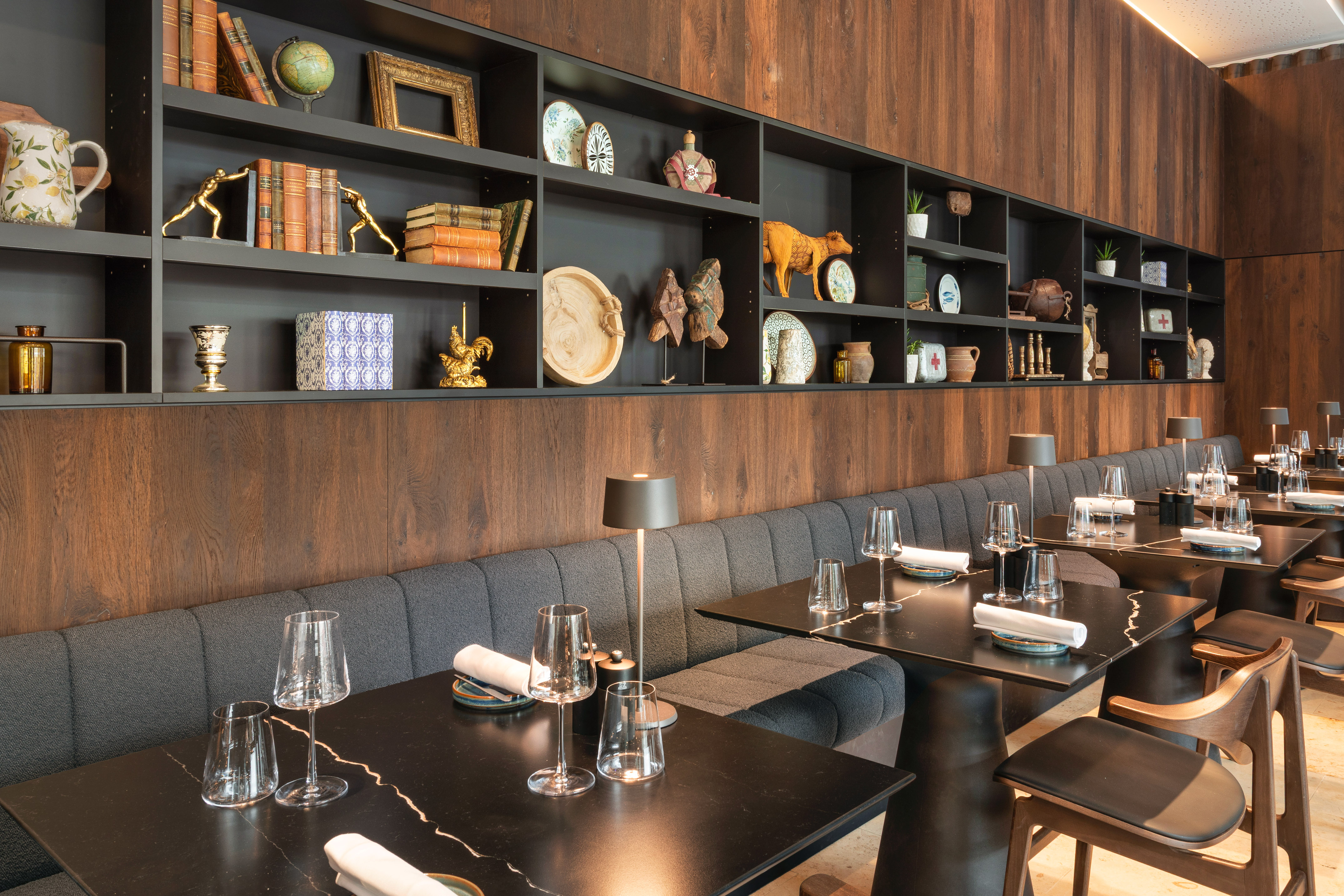 Restaurant interior with decorative wall shelves, dark tables, and booth seating.