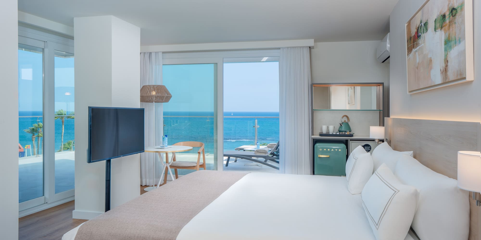 Modern hotel room with king bed, ocean view balcony, and stylish coastal decor.