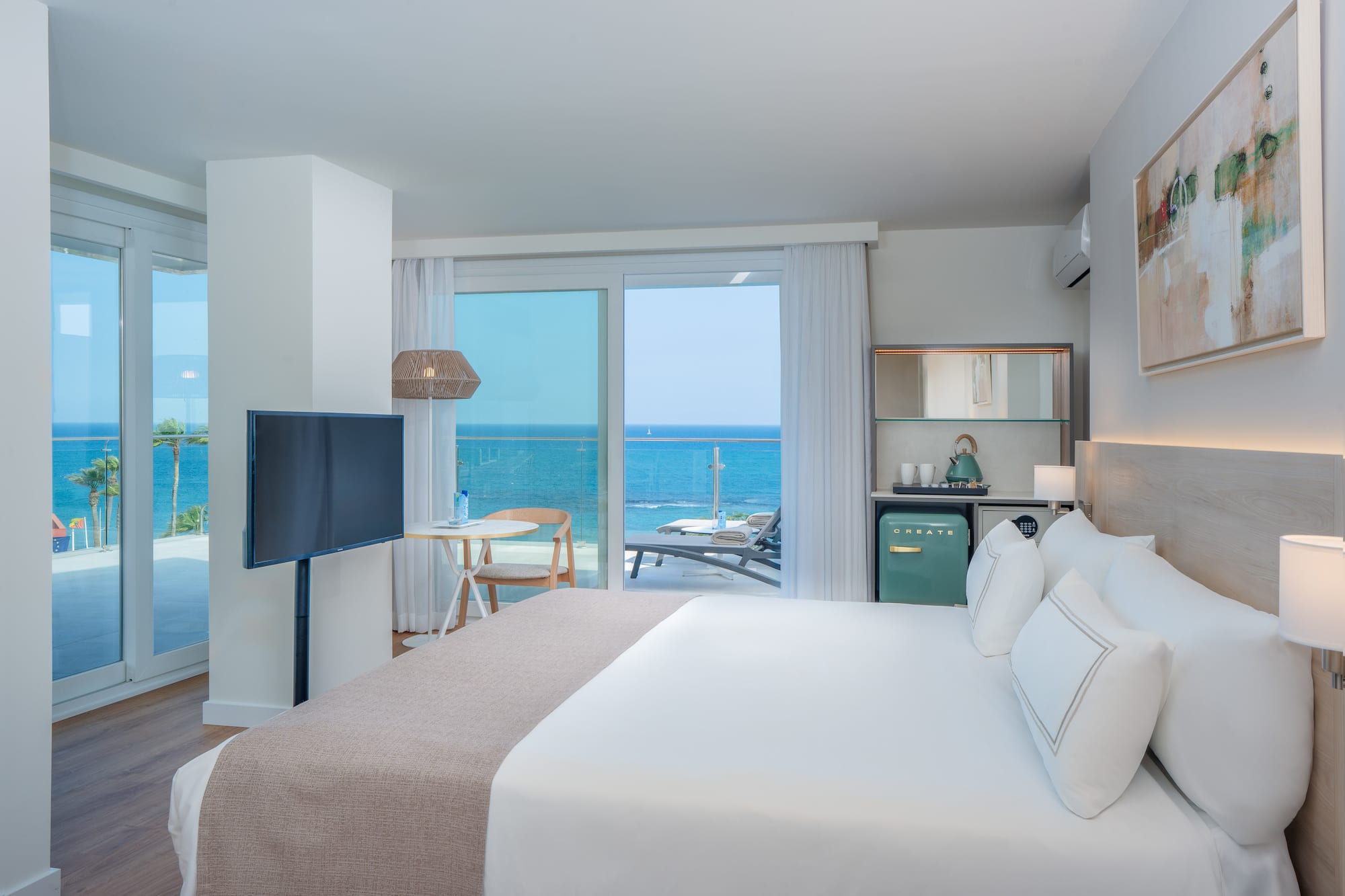 Modern hotel room with king bed, ocean view balcony, and stylish coastal decor.