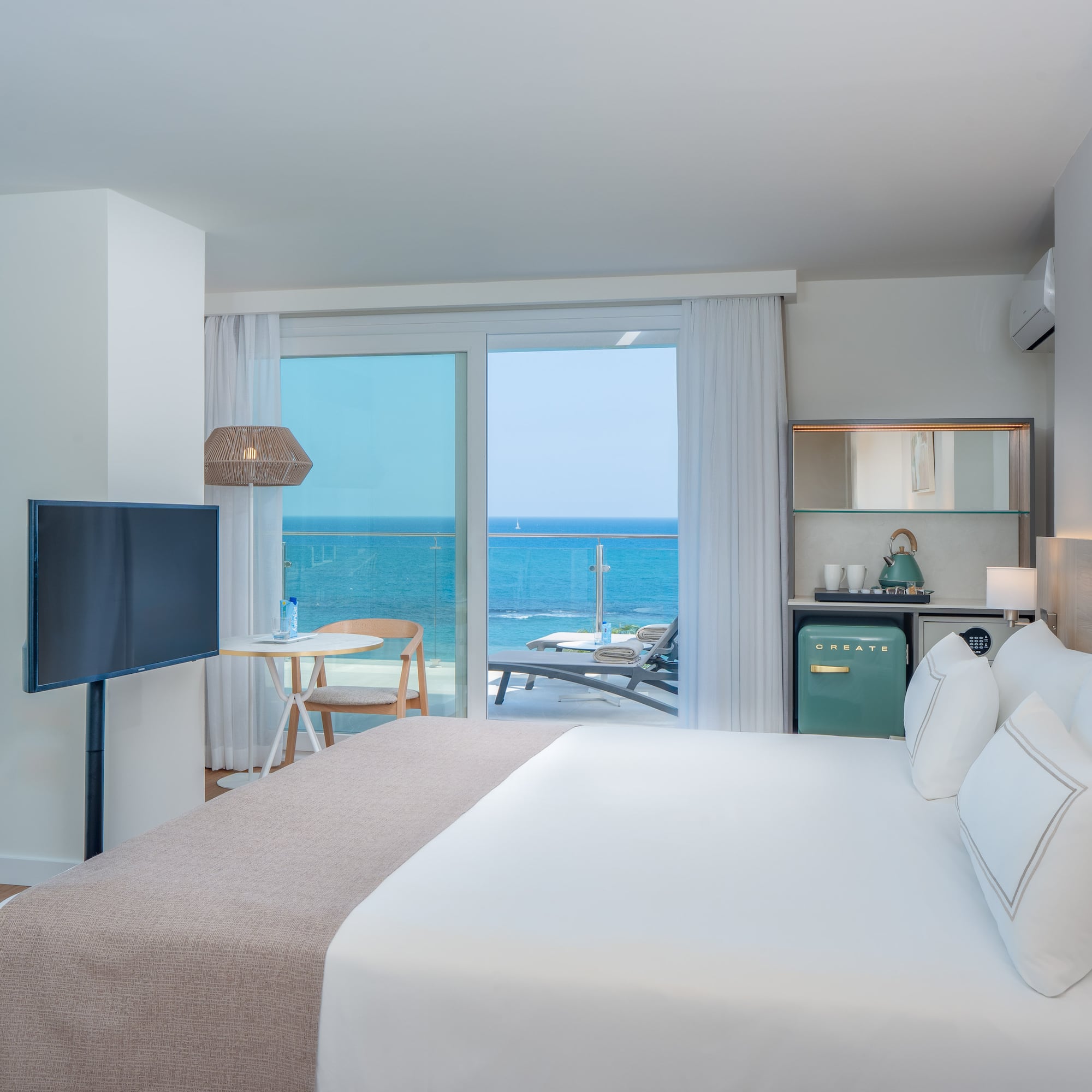 Modern hotel room with king bed, ocean view balcony, and stylish coastal decor.