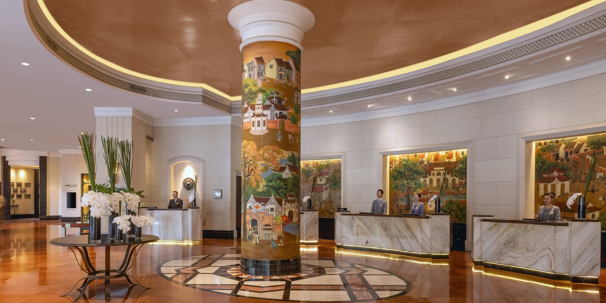 a lobby with a pillar and a table and people standing around