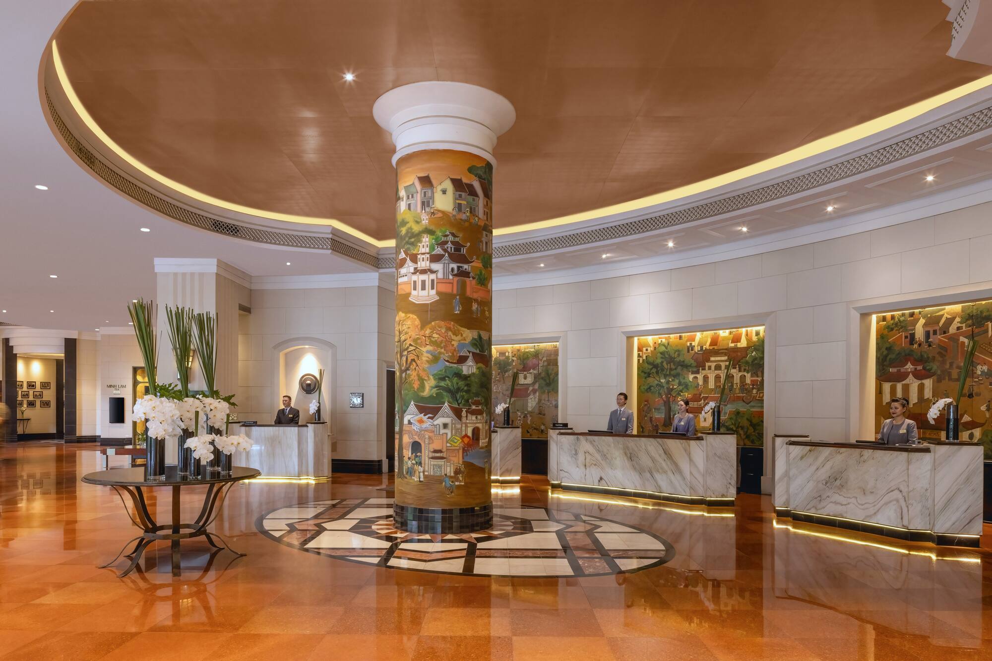 a lobby with a pillar and a table and people standing around