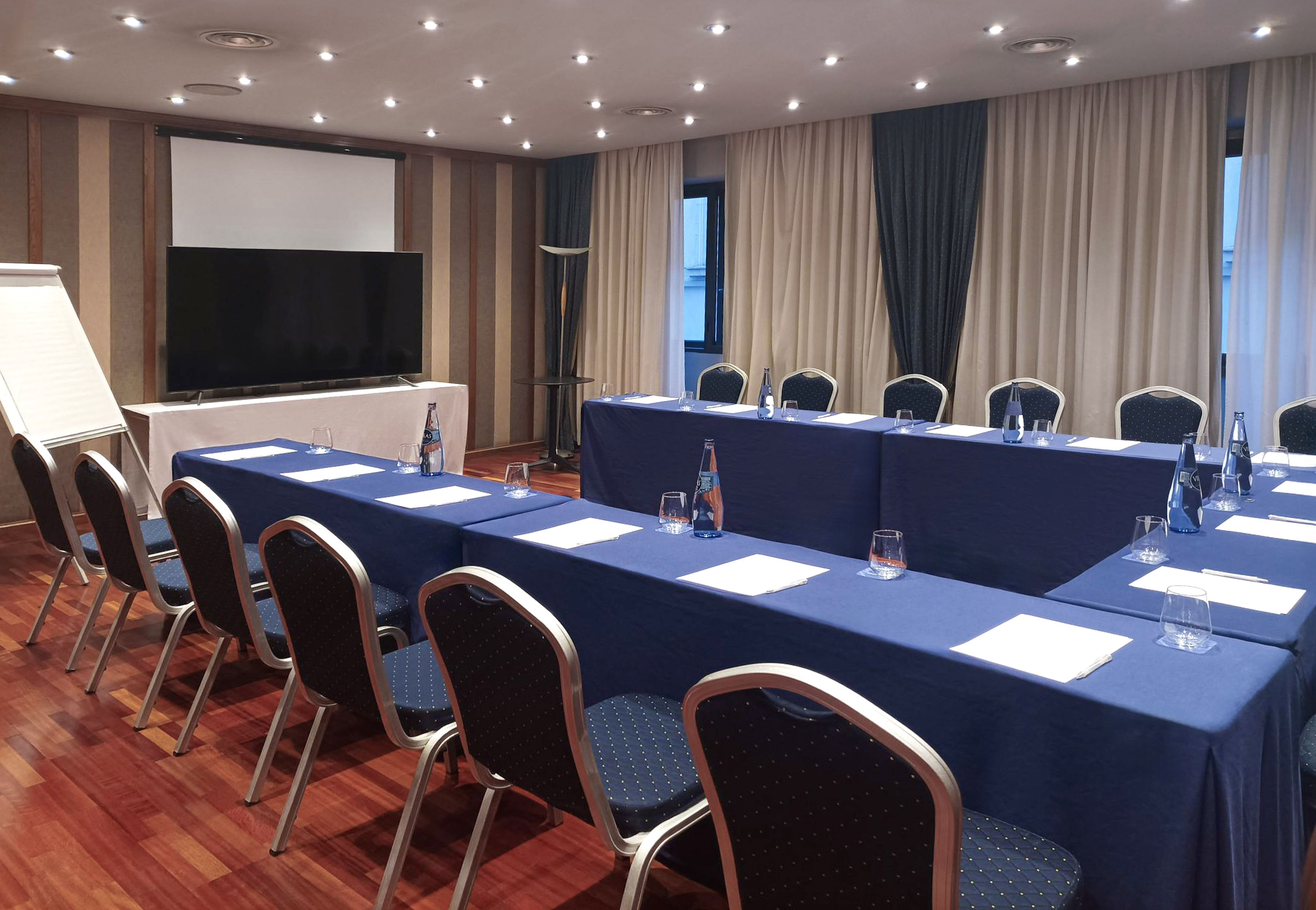 U-shaped conference room with blue tables, chairs, projector screen, and TV.