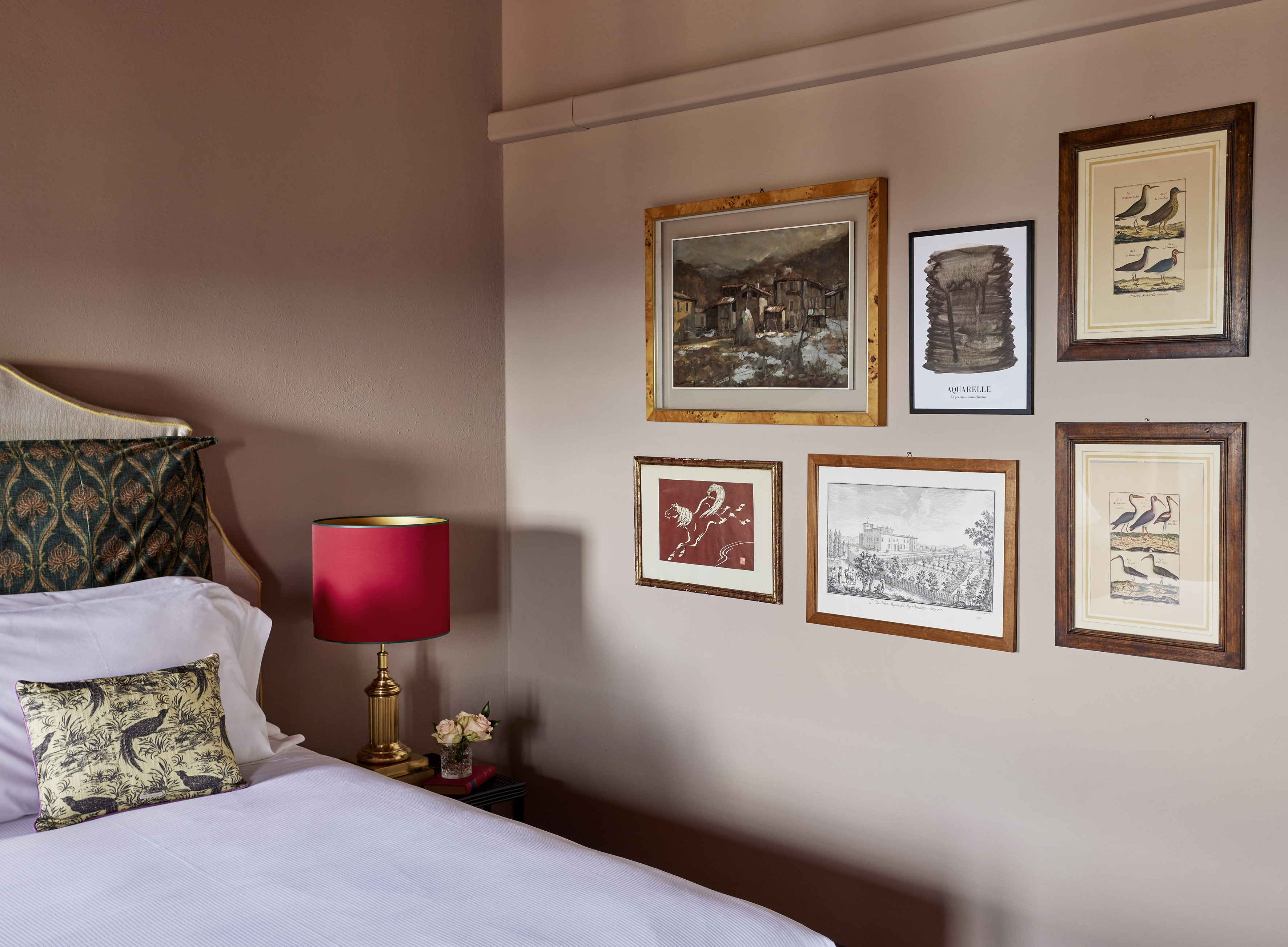 Cozy bedroom with patterned headboard, red lamp, and framed art gallery wall.