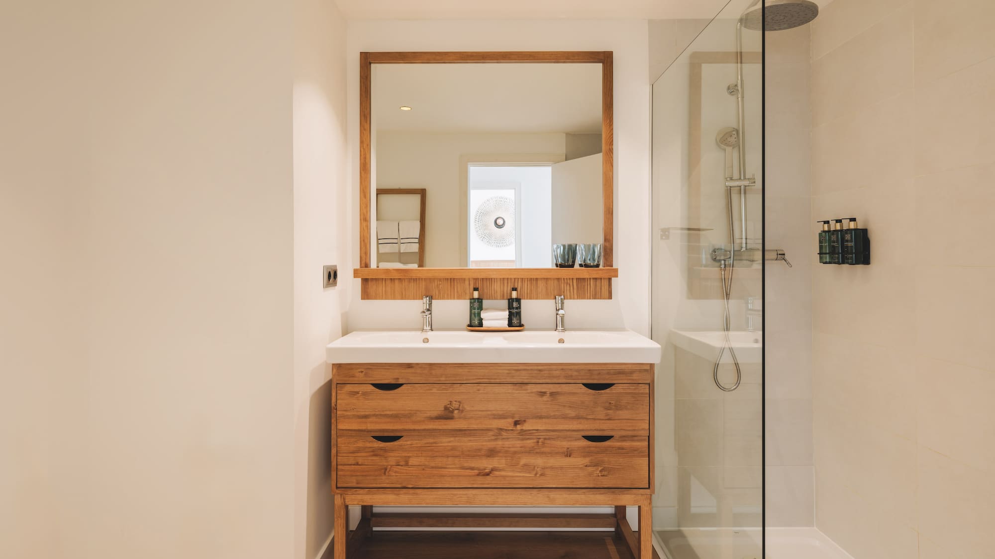 Modern bathroom with wood double vanity, double sink, mirror, and glass shower.