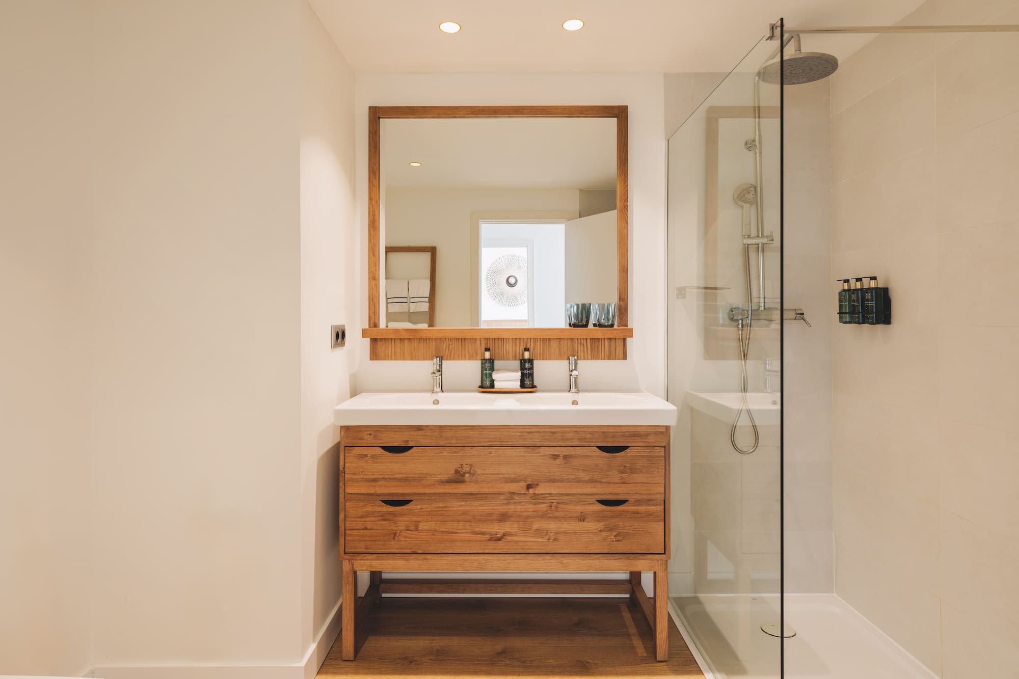Modern bathroom with wood double vanity, double sink, mirror, and glass shower.