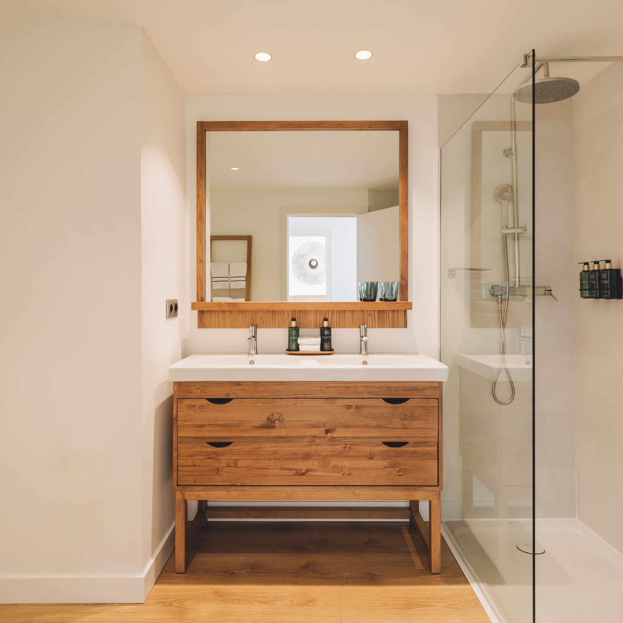Modern bathroom with wood double vanity, double sink, mirror, and glass shower.