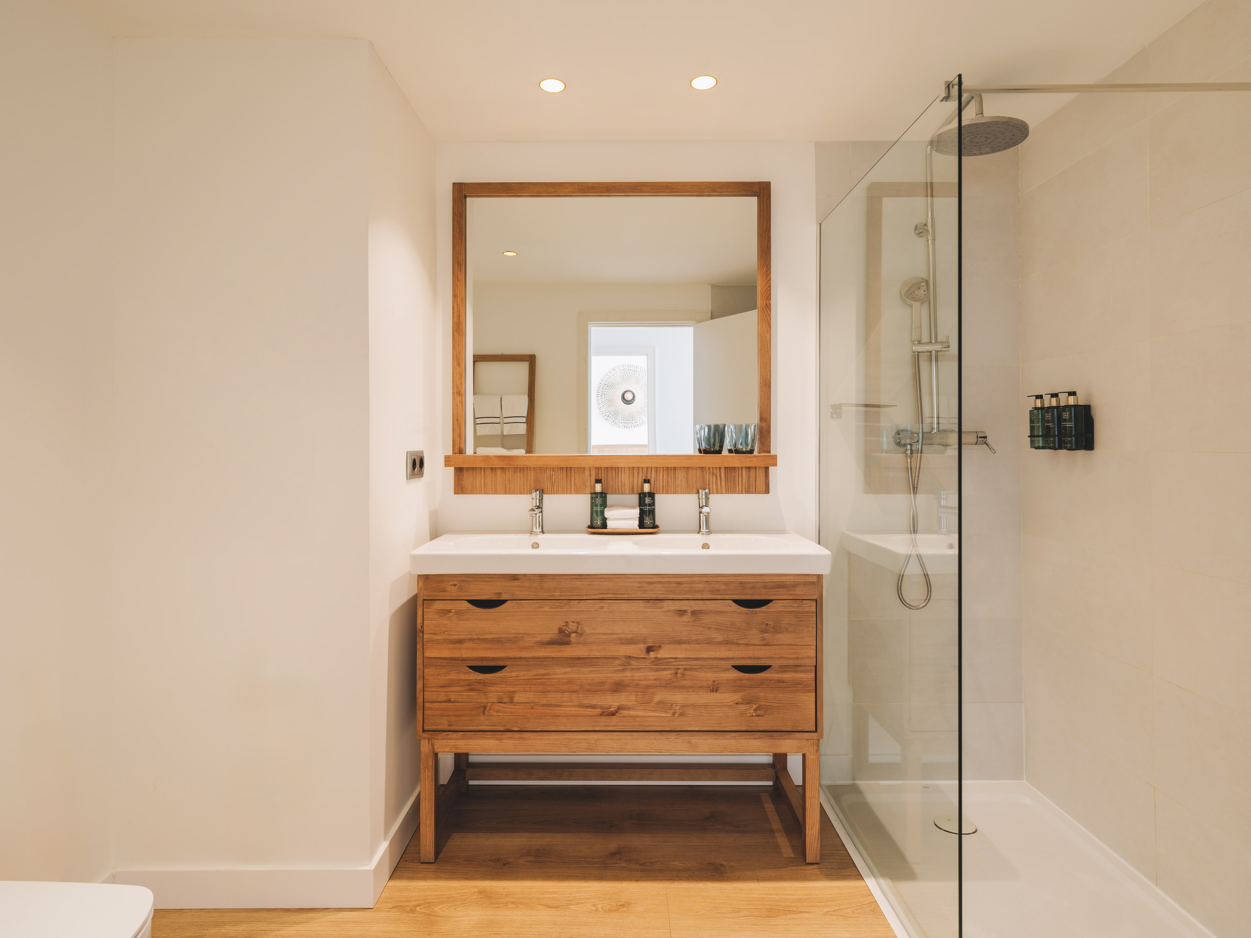 Modern bathroom with wood double vanity, double sink, mirror, and glass shower.