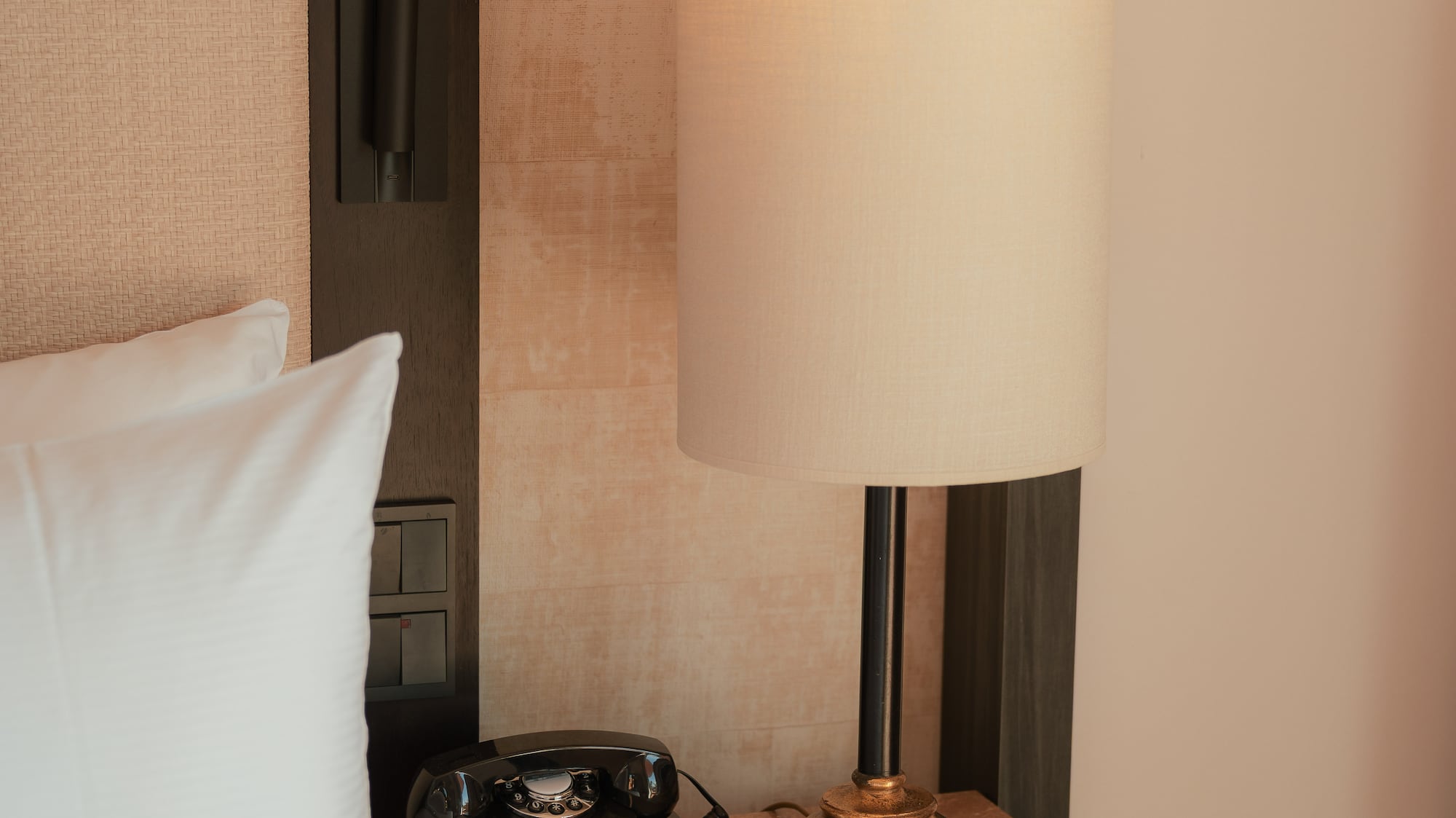 Hotel room bedside table with vintage rotary phone, illuminated lamp, notepad.