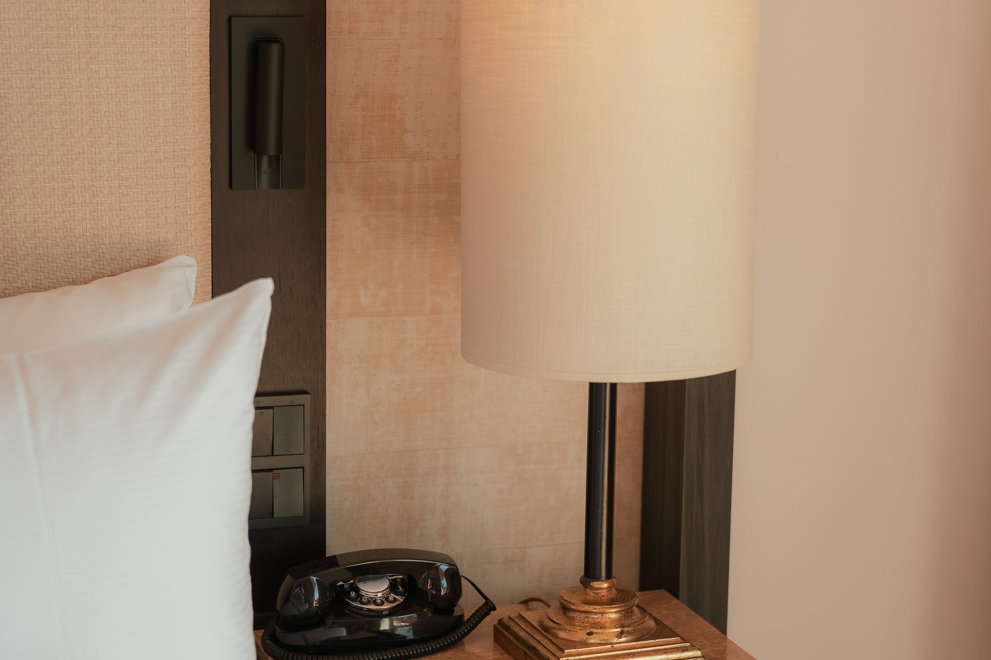 Hotel room bedside table with vintage rotary phone, illuminated lamp, notepad.