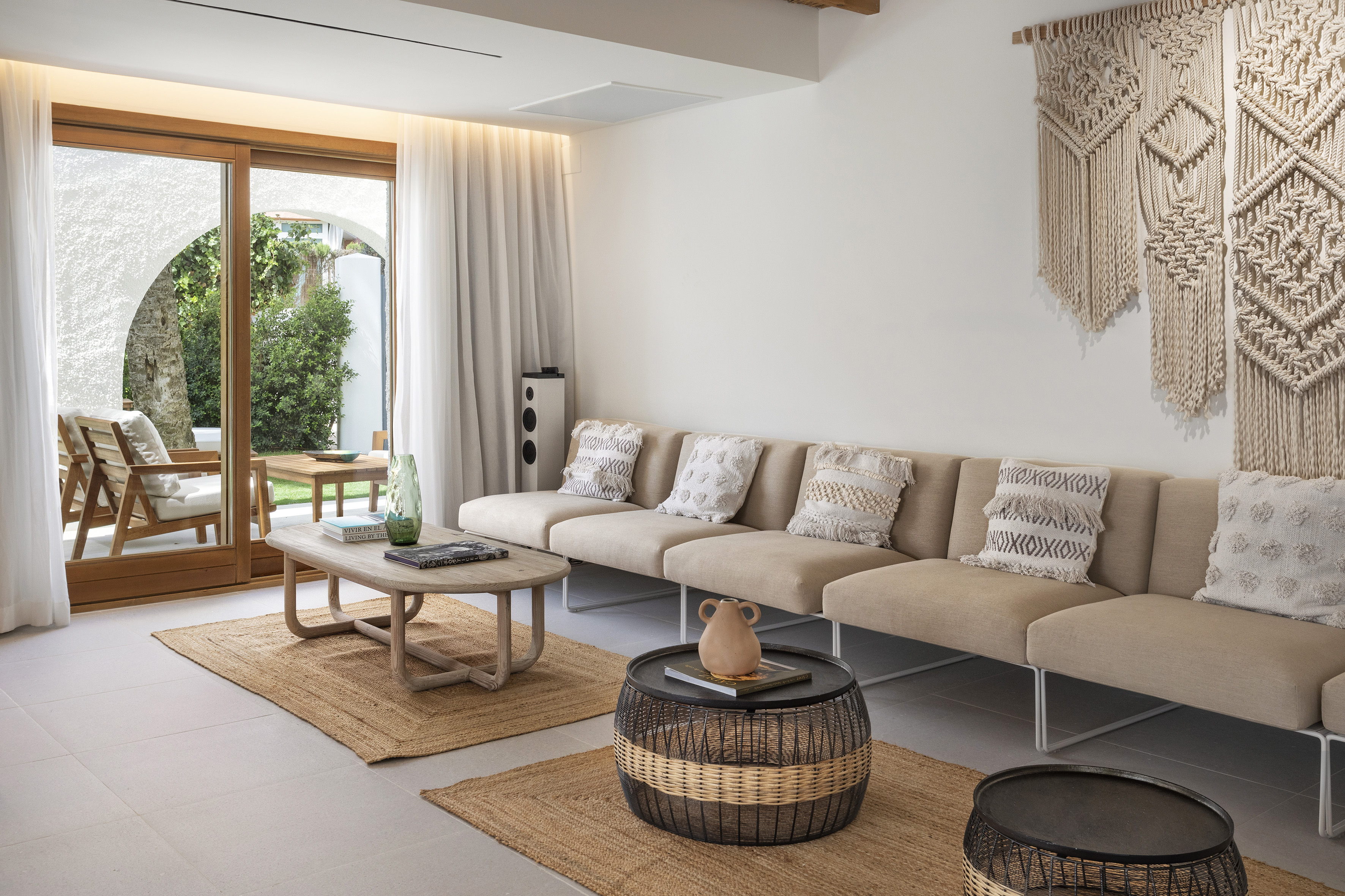 Modern neutral living room with sofa, macrame wall art, and patio garden view.