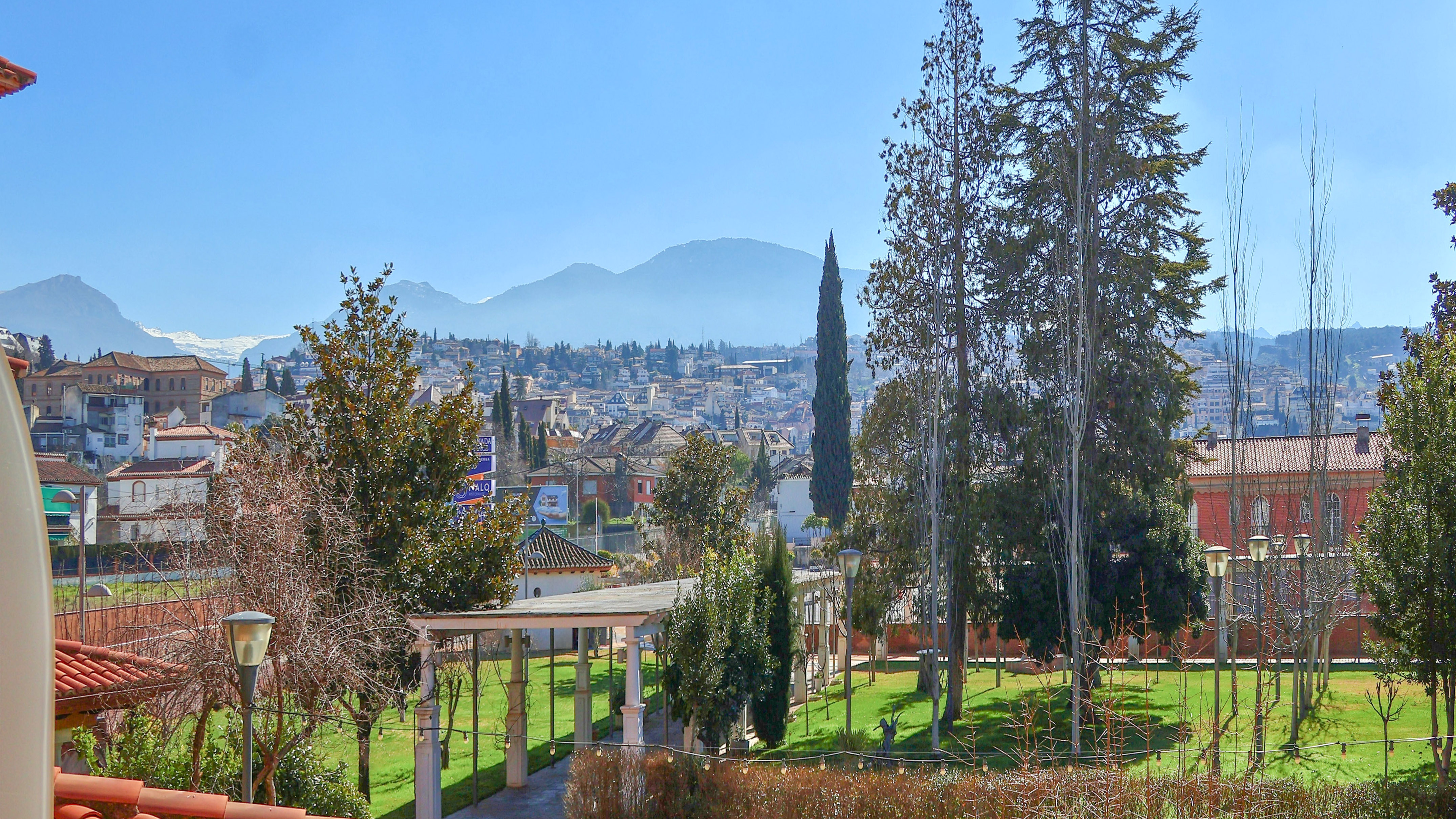 Granada cityscape, green park, and snow-capped Sierra Nevada mountains.