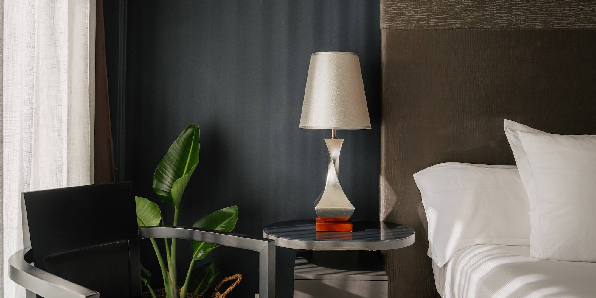 Dormitorio moderno con cama, mesita de noche, lámpara y silla elegante.