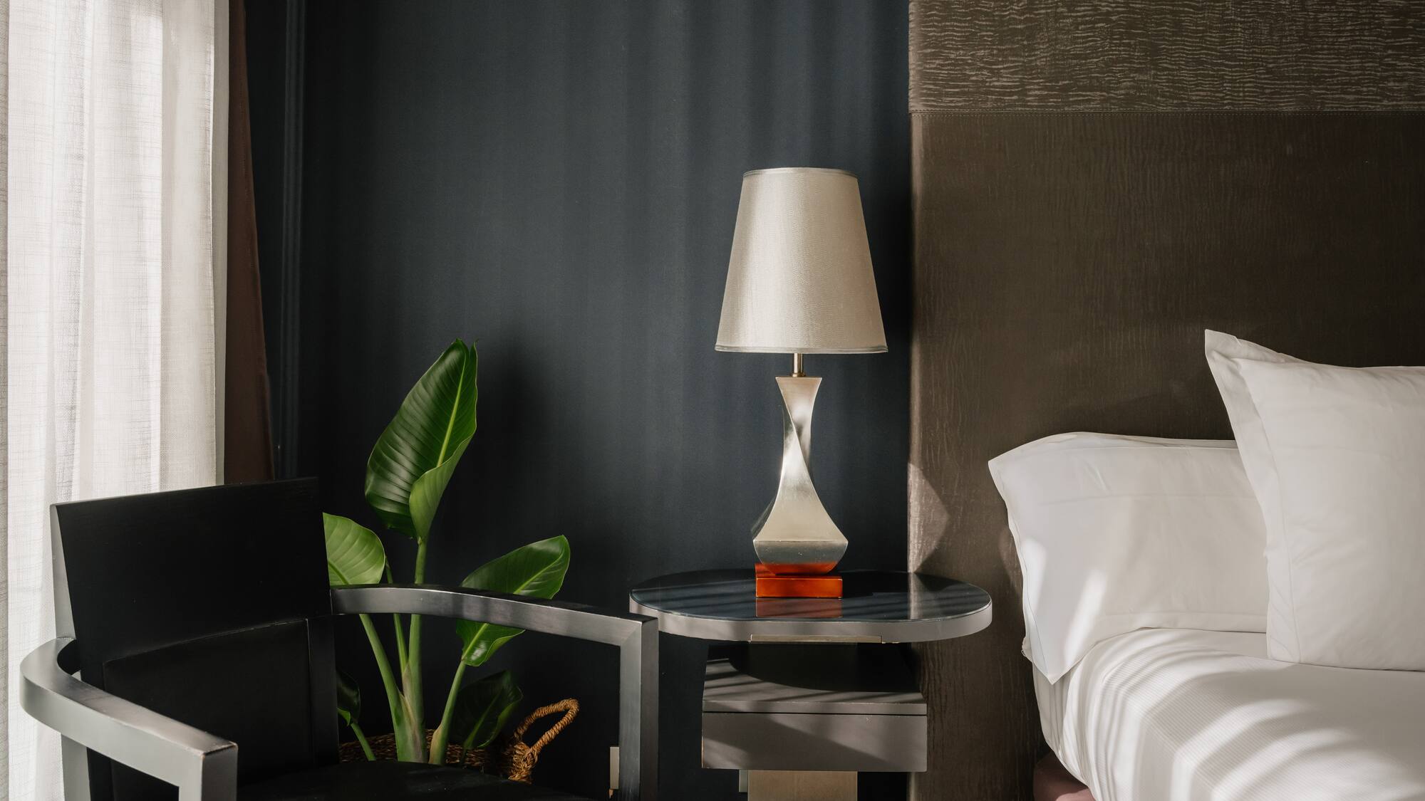 Dormitorio moderno con cama, mesita de noche, lámpara y silla elegante.