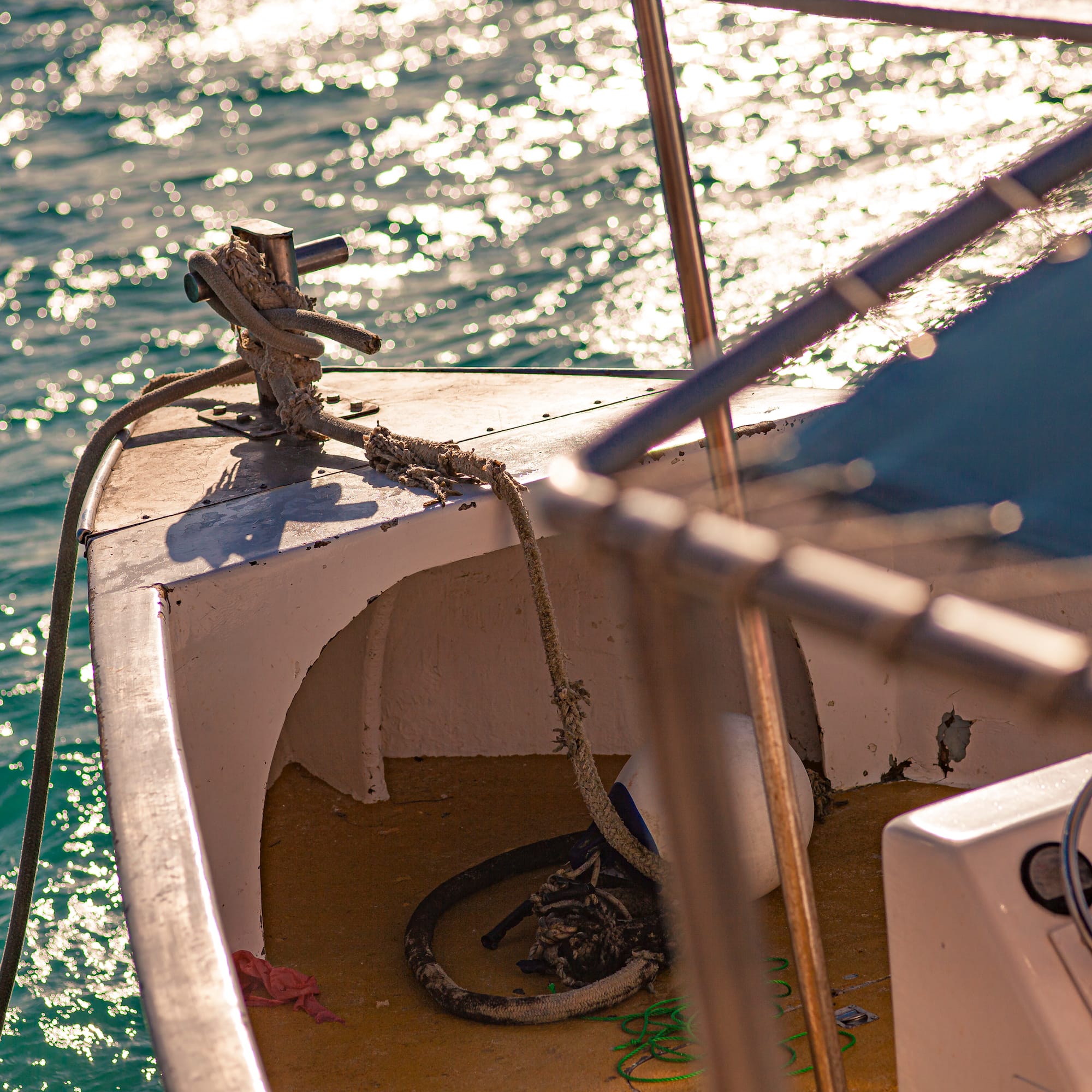 Boat bow with rope and cleat on sparkling blue ocean water.