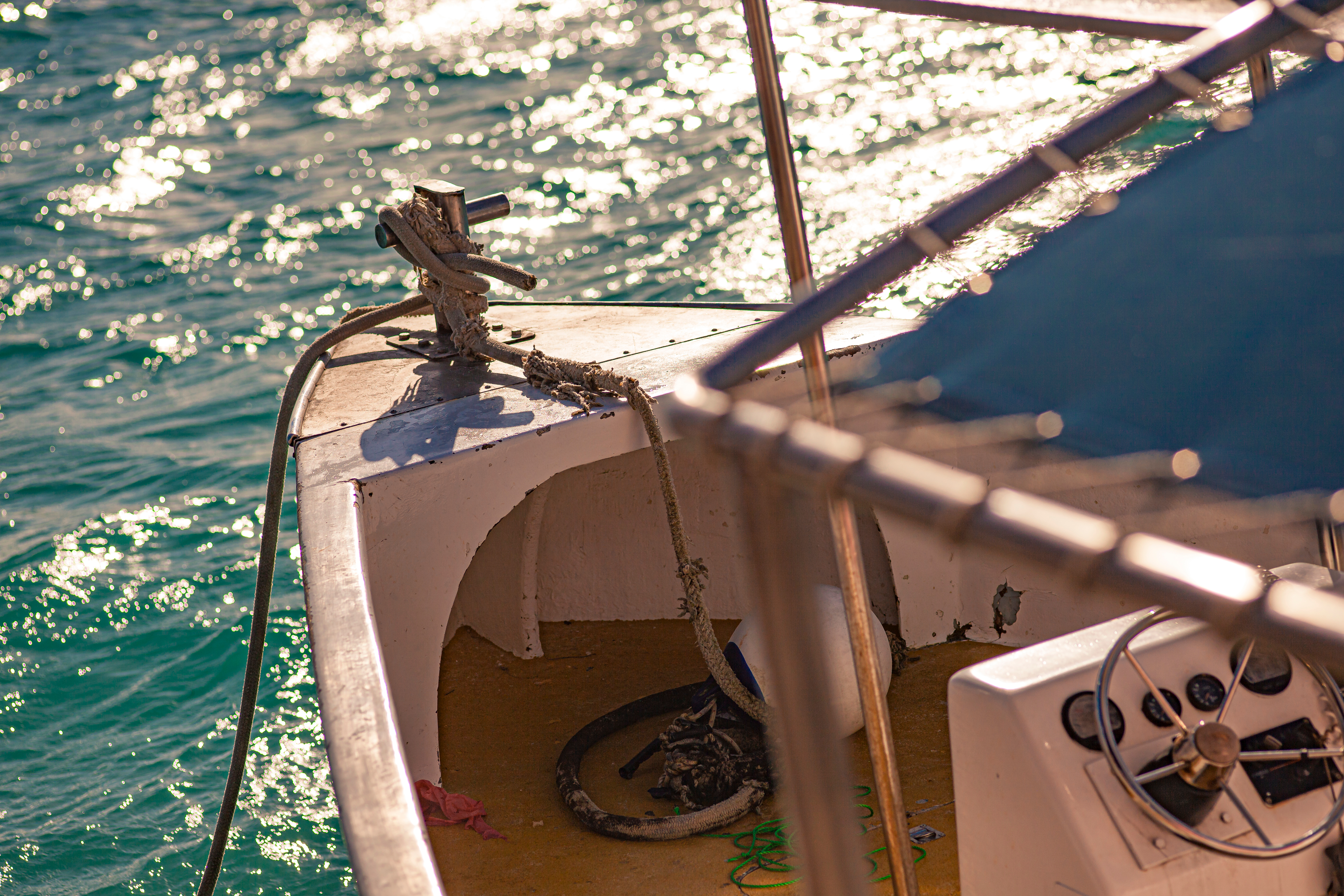 Boat bow with rope and cleat on sparkling blue ocean water.