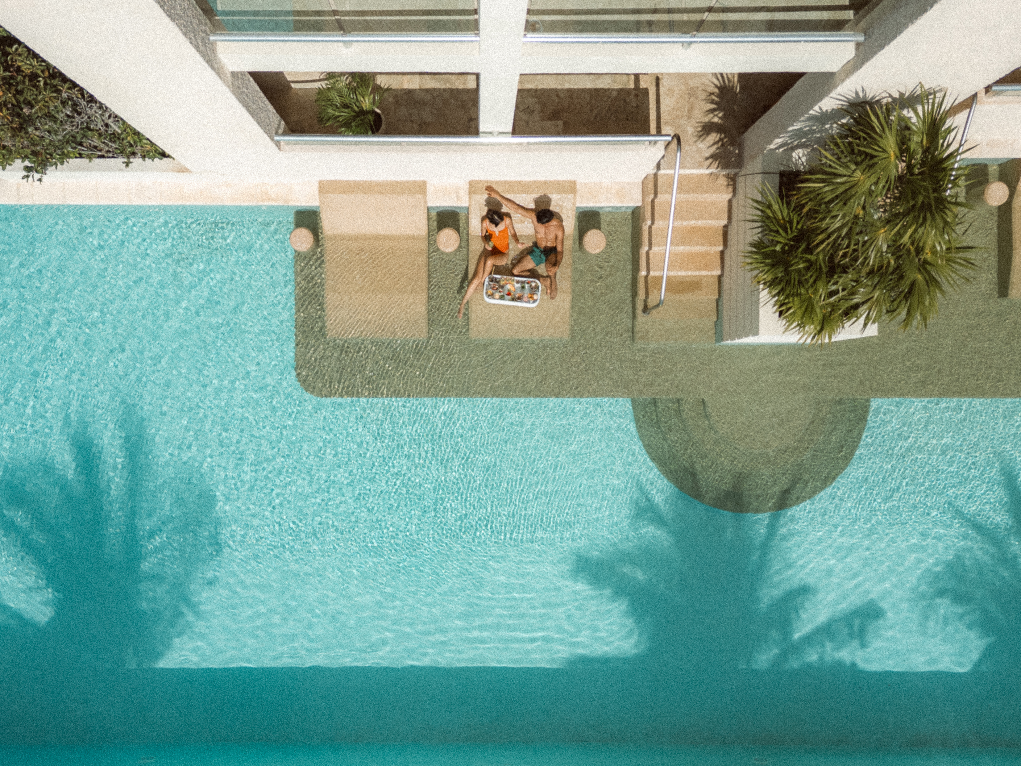 a man and woman sitting on a lounge chair next to a pool