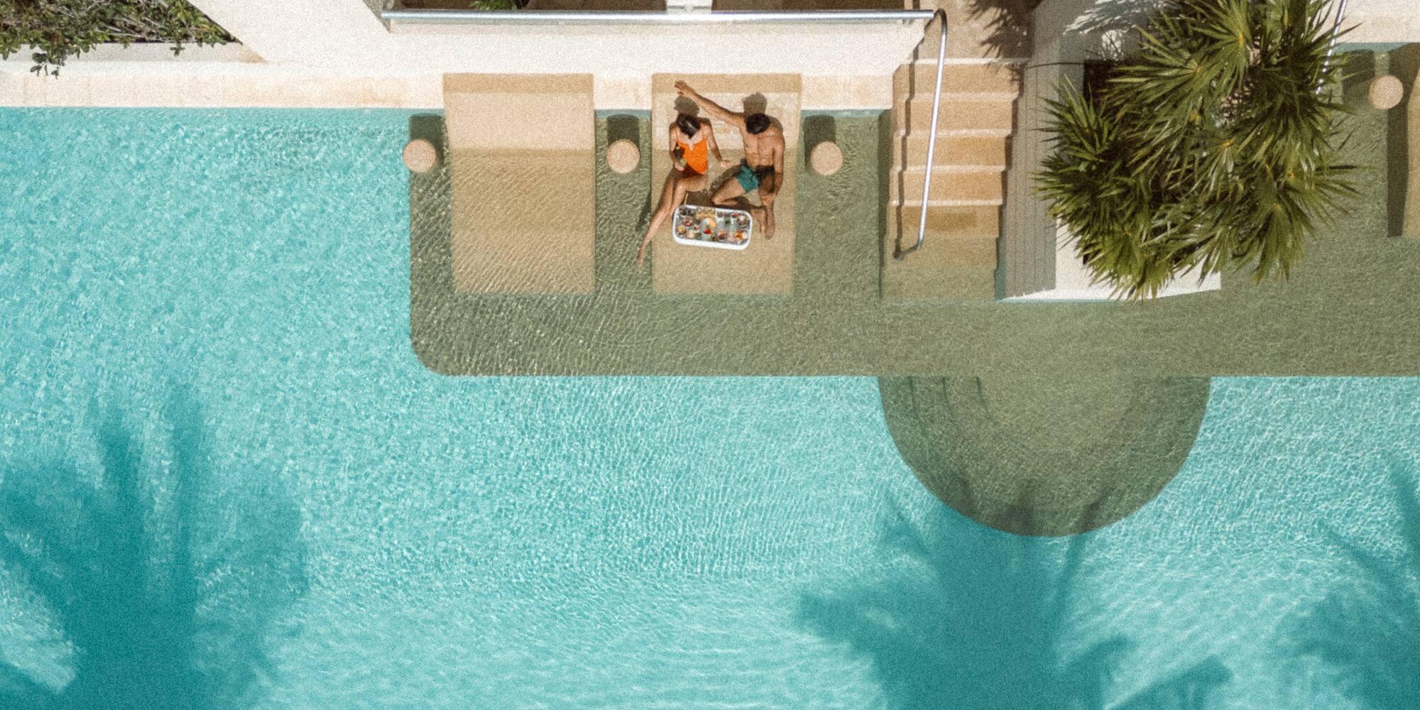 a man and woman sitting on a lounge chair next to a pool