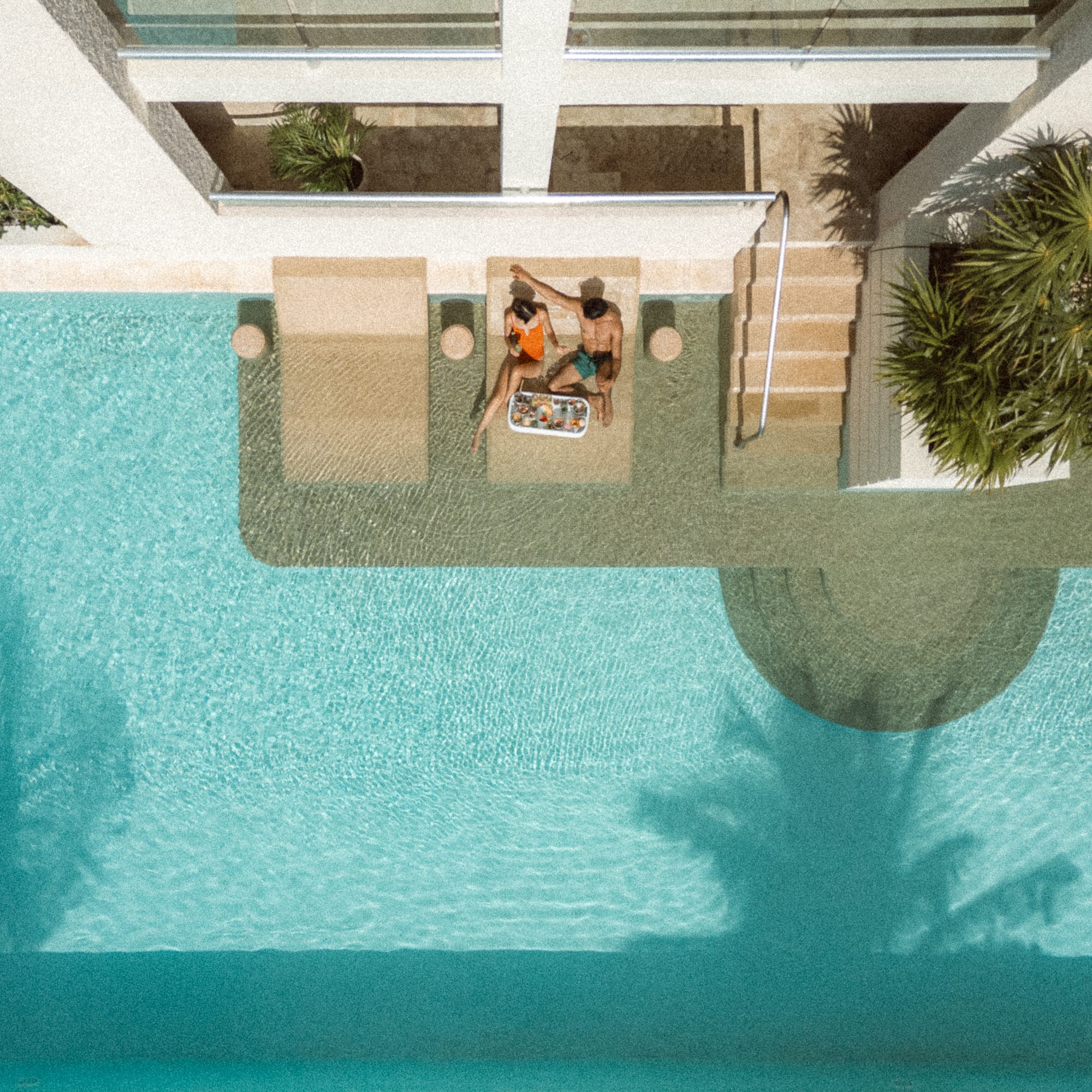 a man and woman sitting on a lounge chair next to a pool