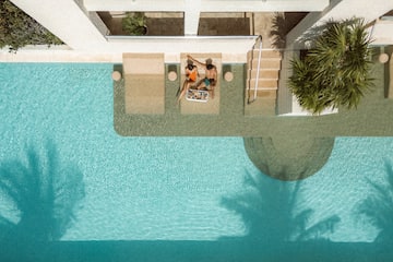 a man and woman sitting on a lounge chair next to a pool