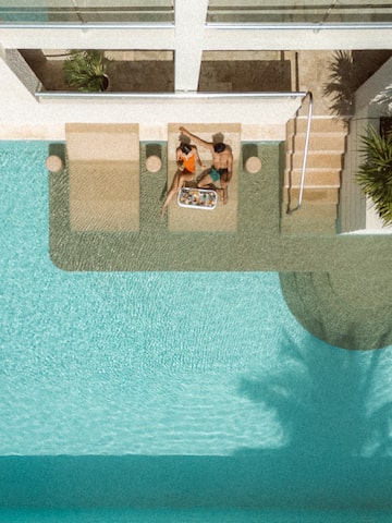 a man and woman sitting on a lounge chair next to a pool