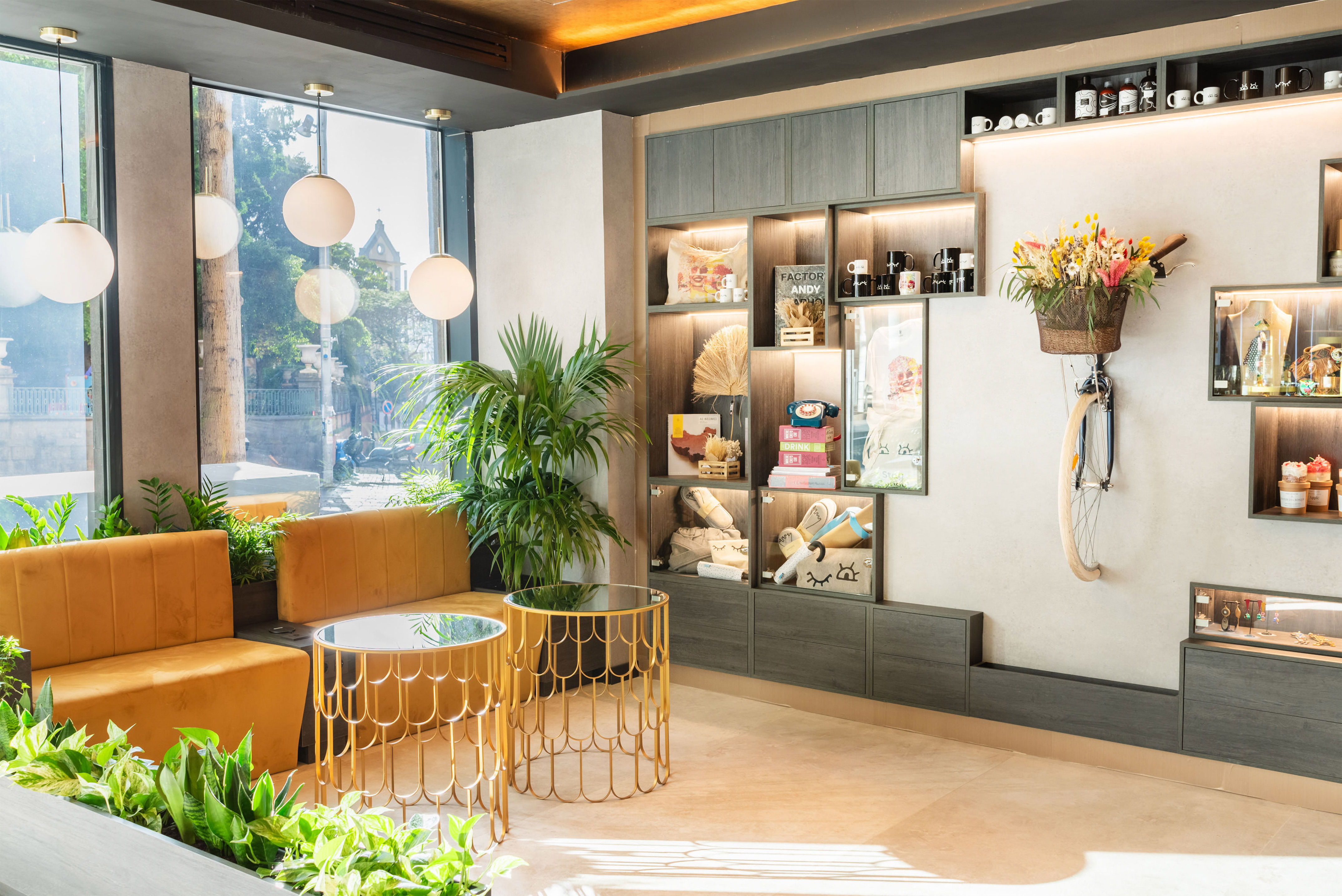 Chic lounge with yellow velvet sofas, green plants, and illuminated retail shelves.