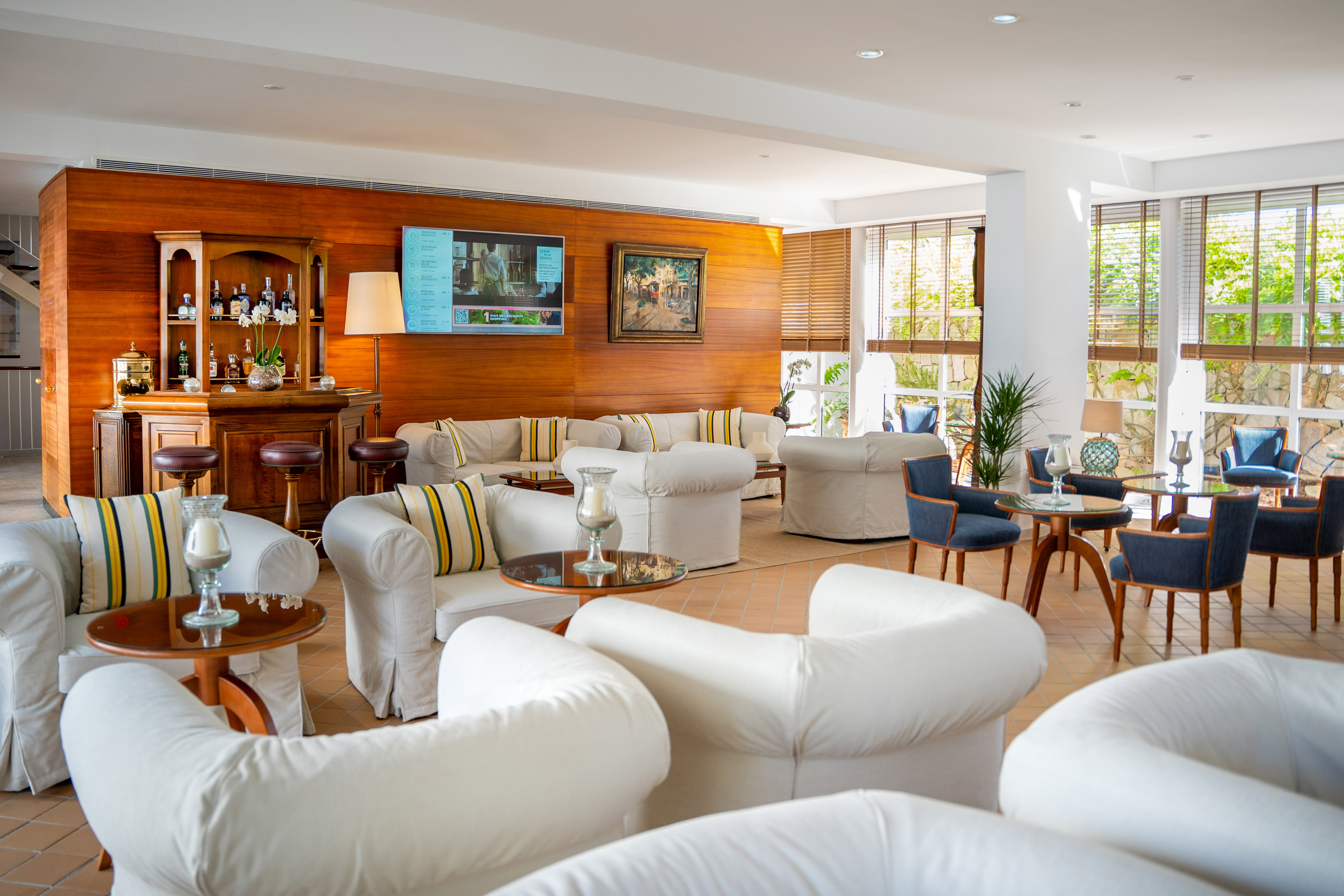 Hotel lounge with wooden bar, white sofas, blue chairs, and natural light.