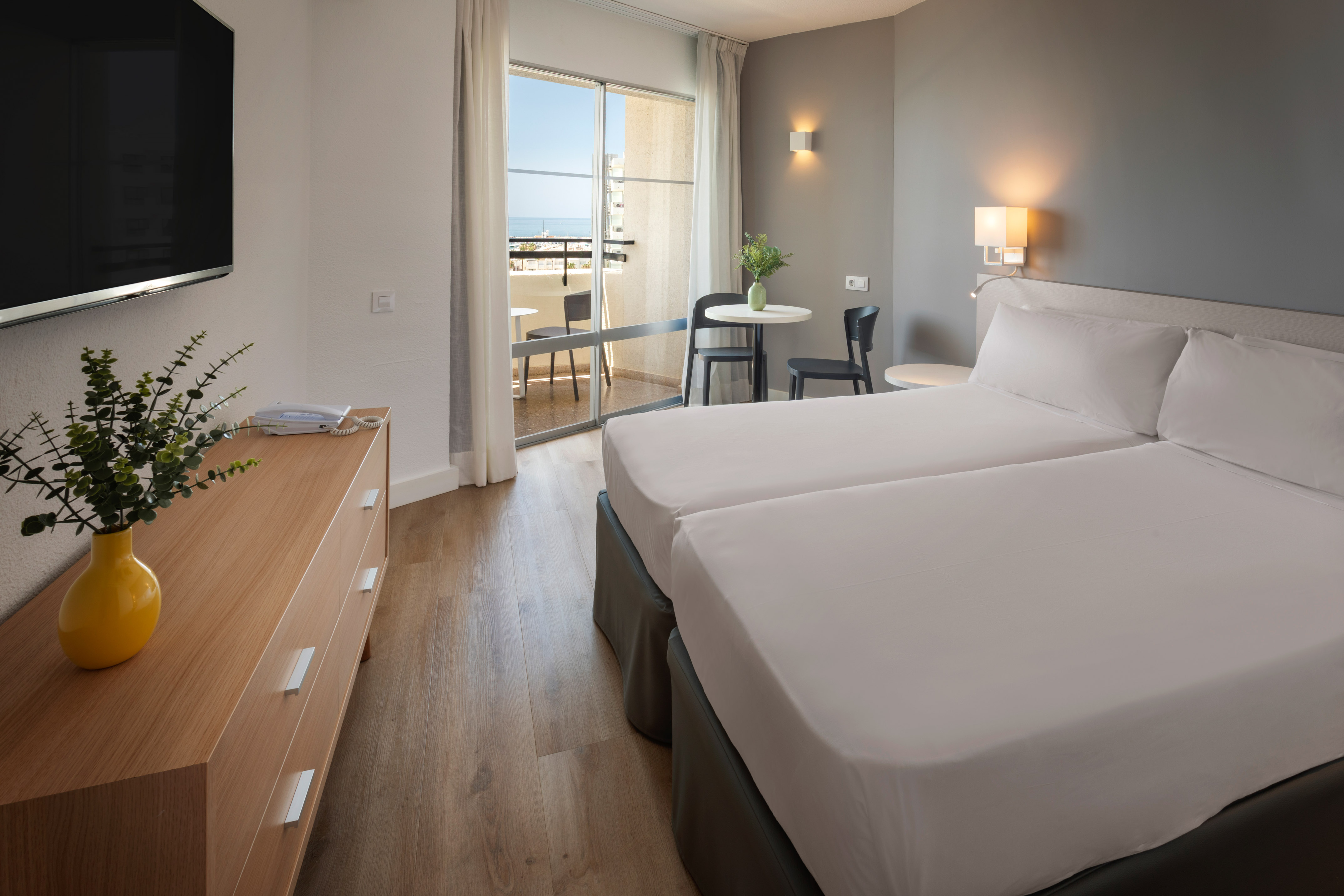 Modern hotel room with twin beds and sea view balcony.