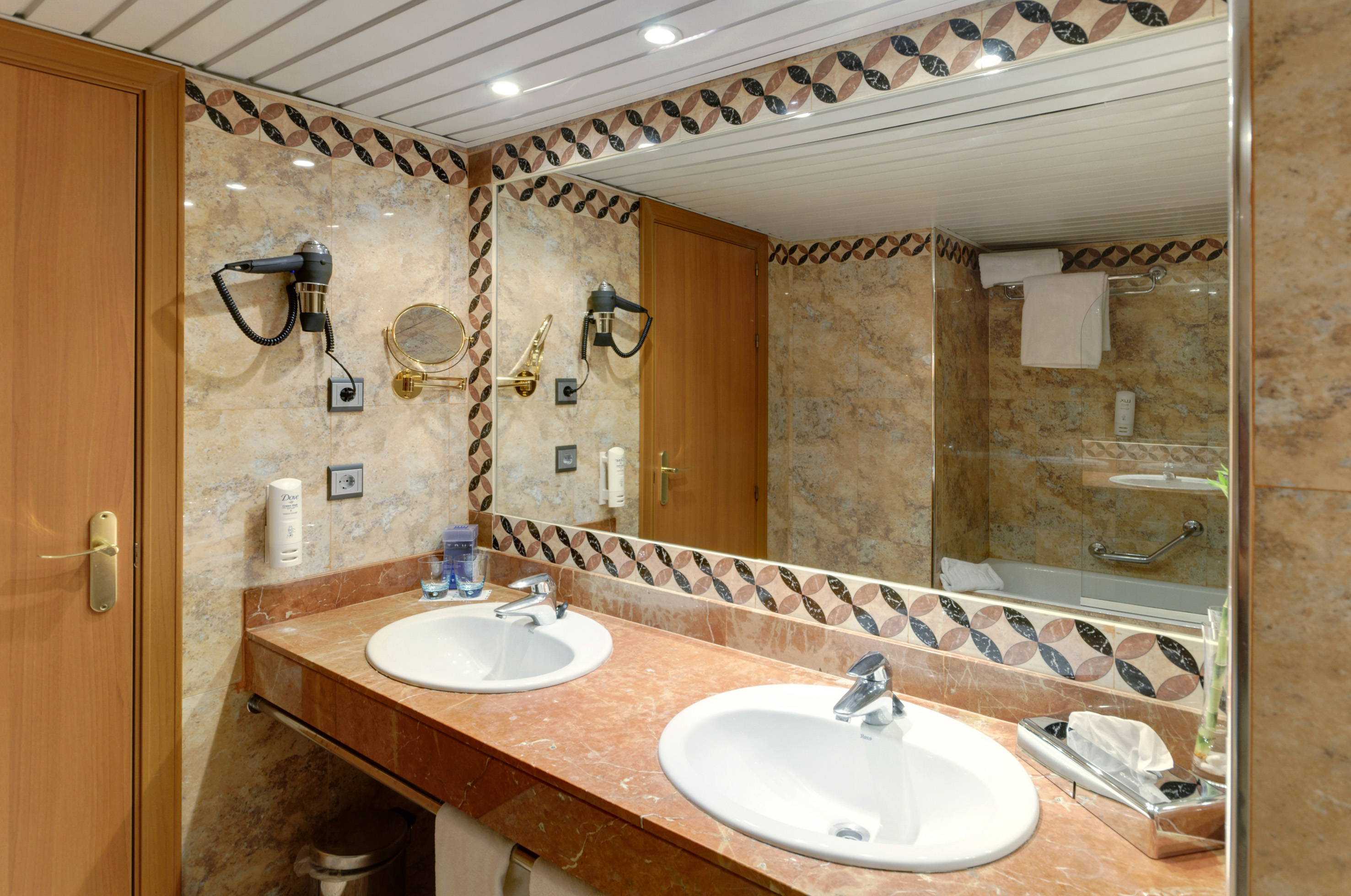 Hotel bathroom with double vanity, red marble counter, patterned tiles, and mirror.