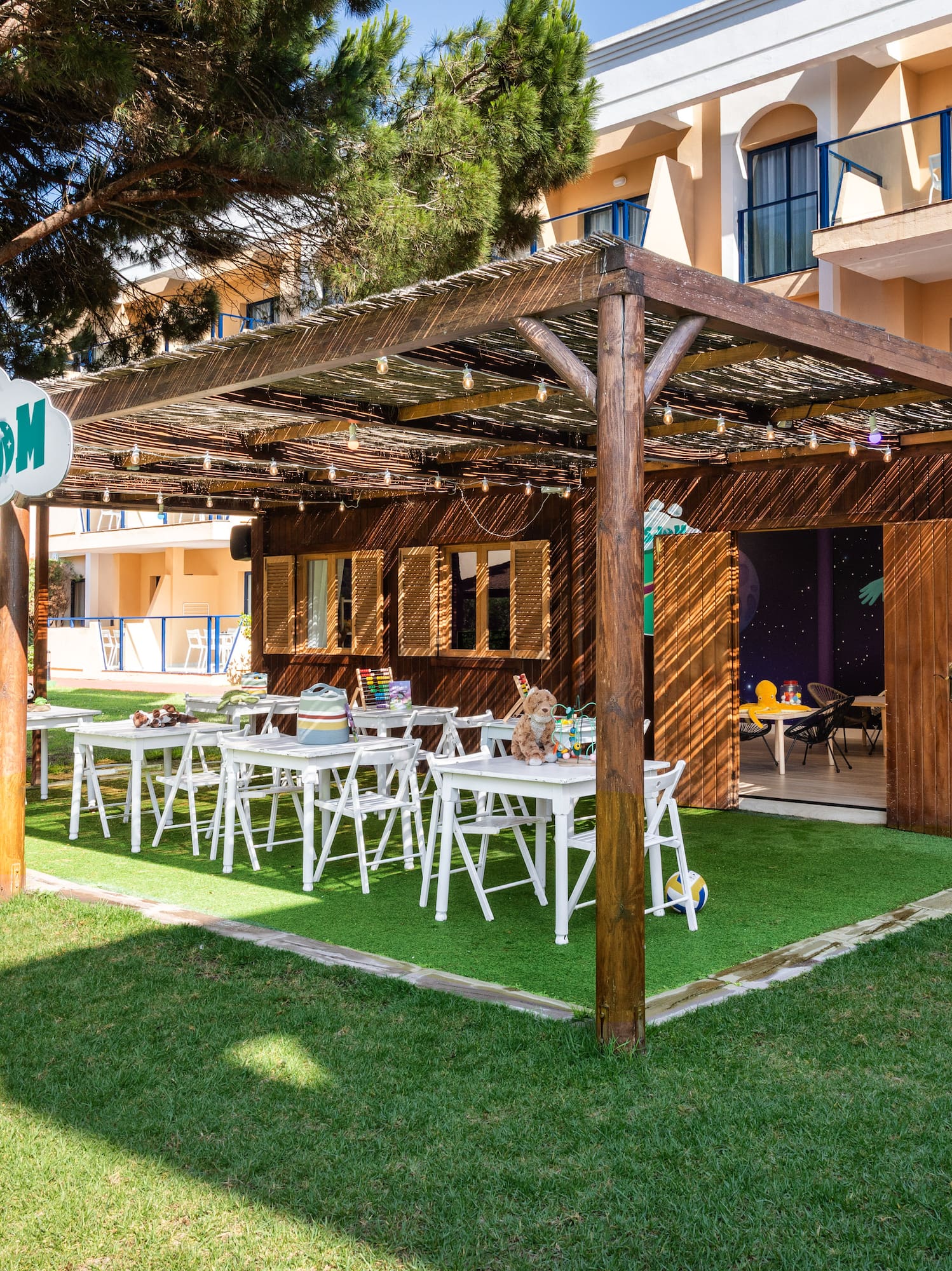 KidsDom outdoor club with wooden shelter, activity tables, and green lawn.